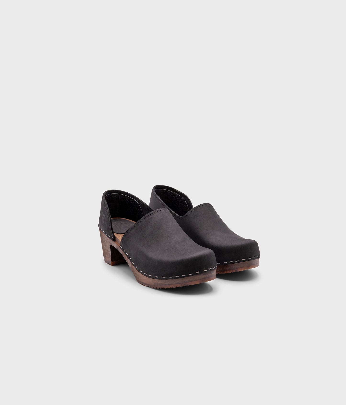 high heeled closed-back clogs in black nubuck leather stapled on a dark wooden base