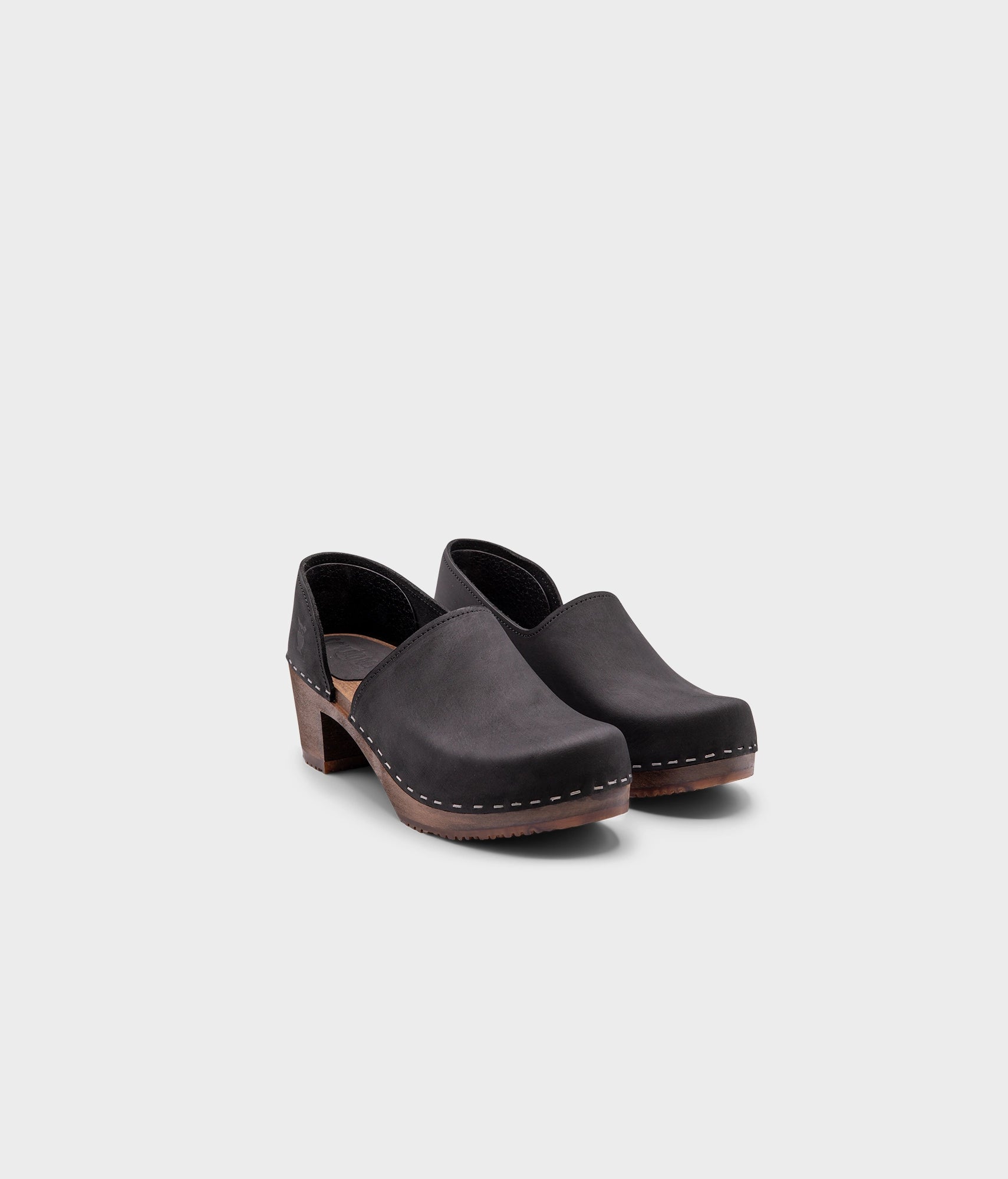 high heeled closed-back clogs in black nubuck leather stapled on a dark wooden base