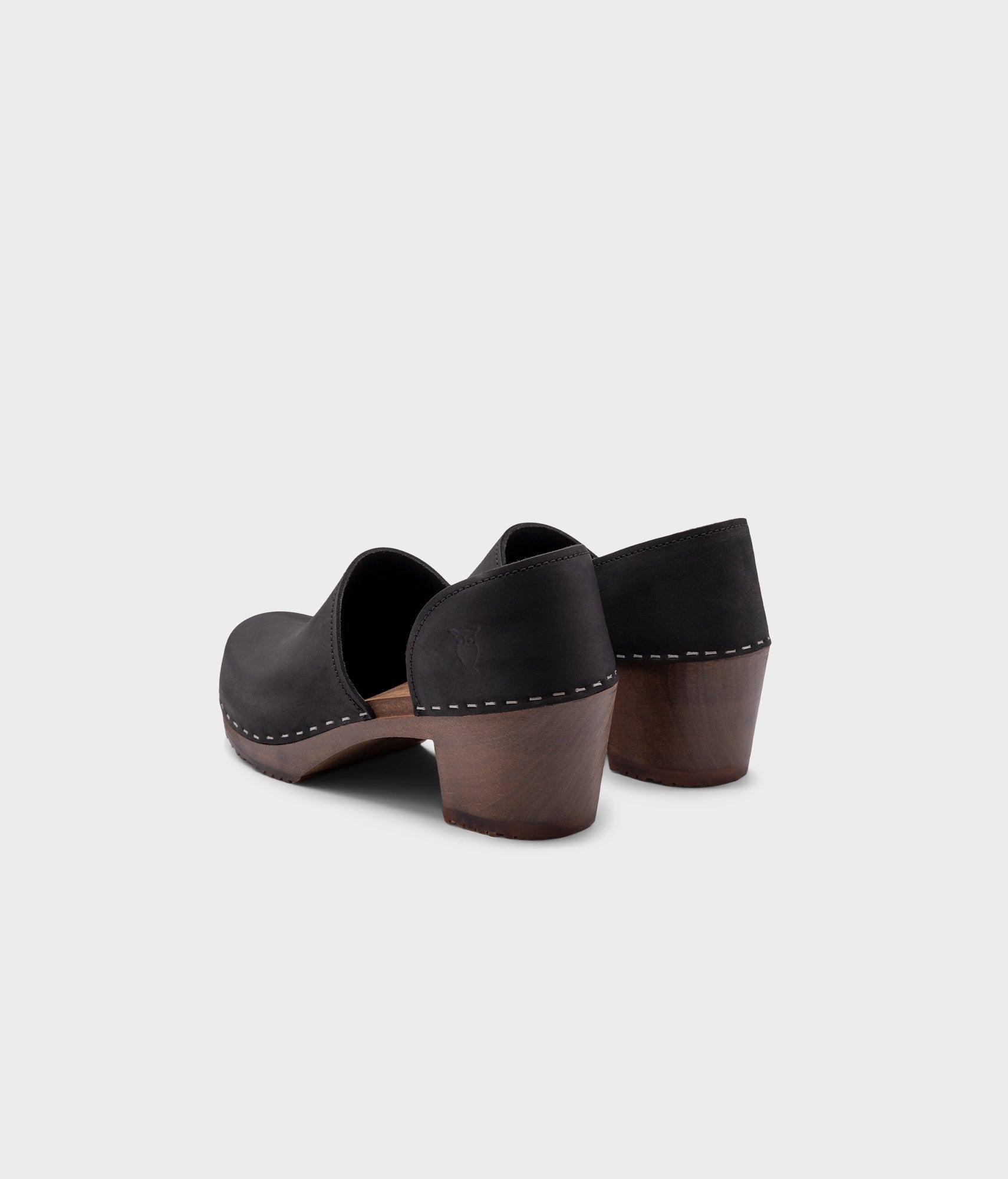 high heeled closed-back clogs in black nubuck leather stapled on a dark wooden base