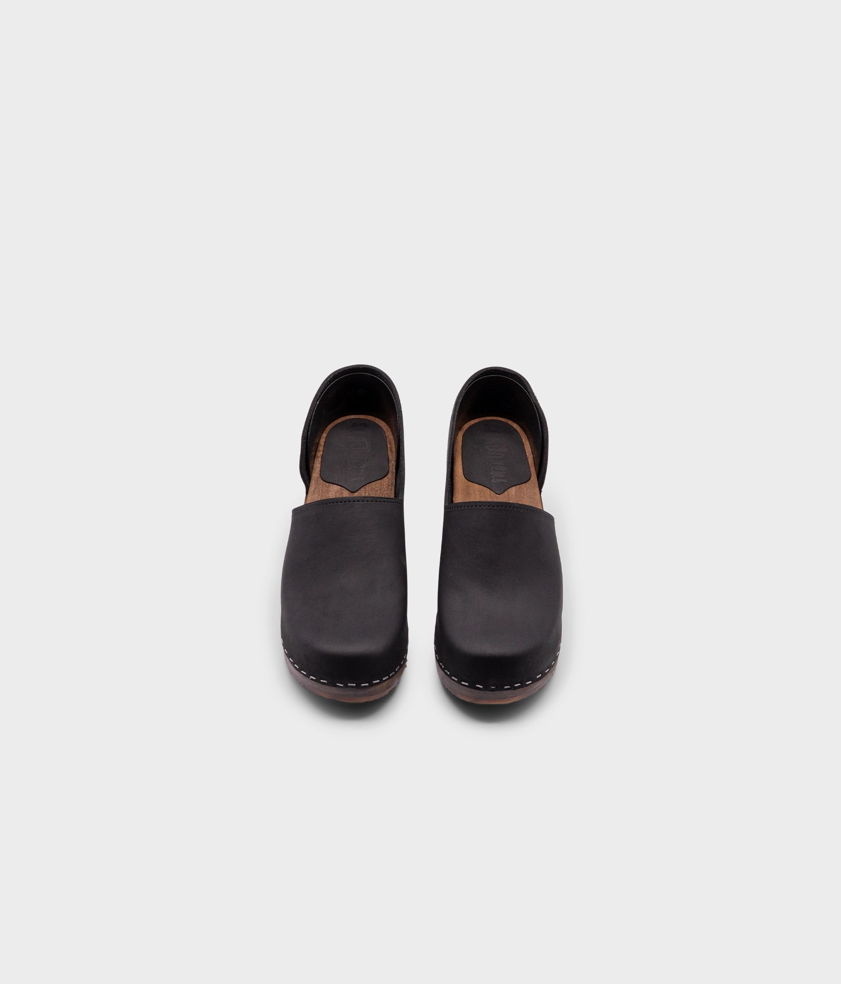 high heeled closed-back clogs in black nubuck leather stapled on a dark wooden base