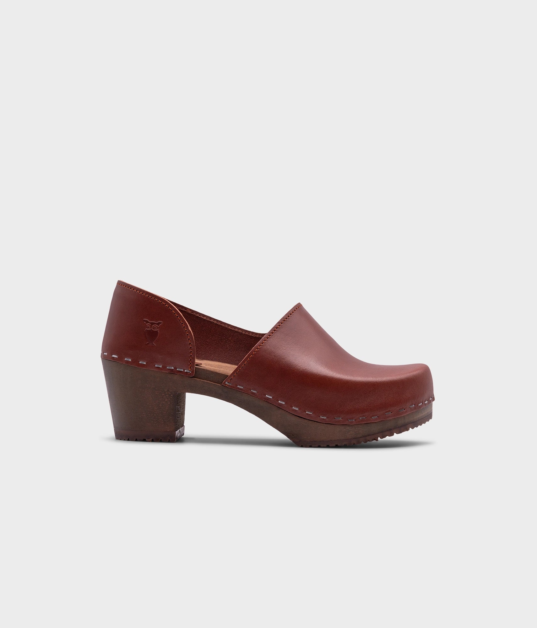high heeled closed-back clogs in cognac red vegetable tanned leather stapled on a dark wooden base