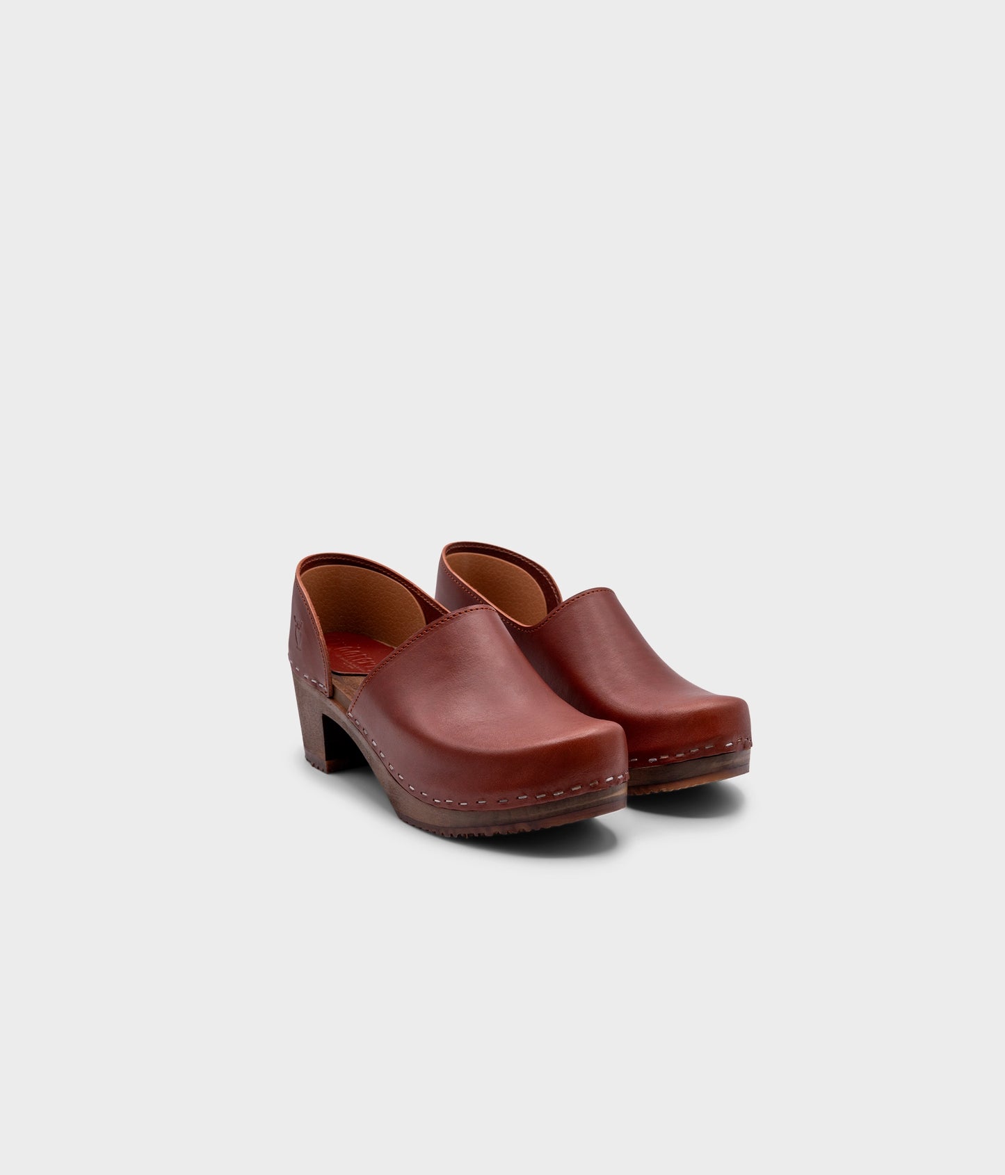 high heeled closed-back clogs in cognac red vegetable tanned leather stapled on a dark wooden base