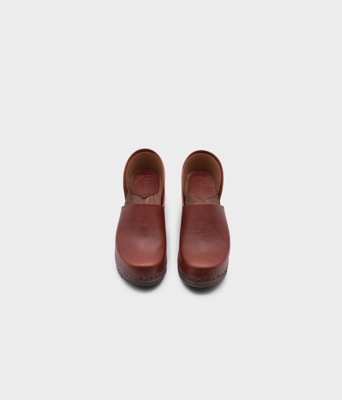 high heeled closed-back clogs in cognac red vegetable tanned leather stapled on a dark wooden base