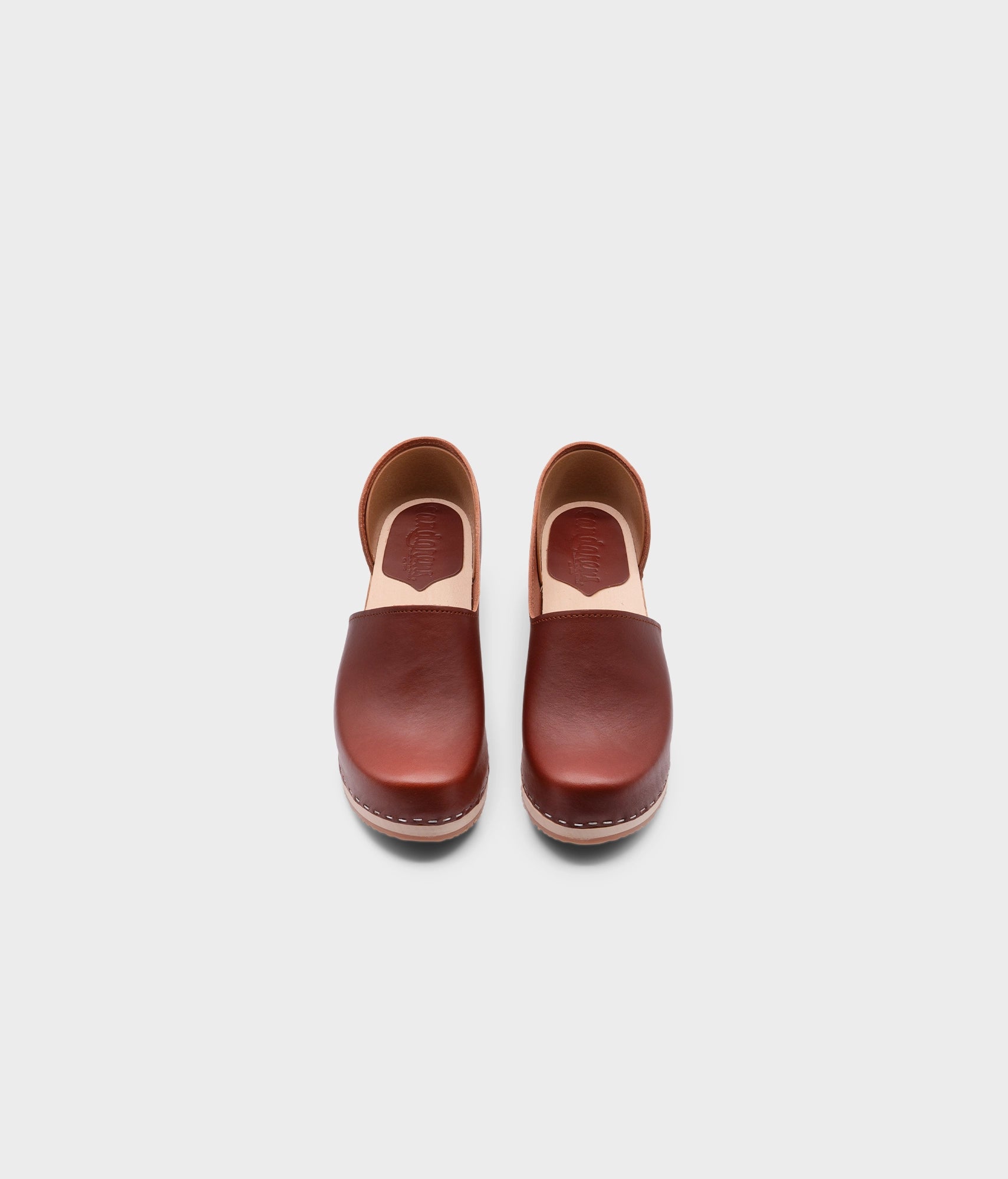 high heeled closed-back clogs in red cognac vegetable tanned leather stapled on a light wooden base