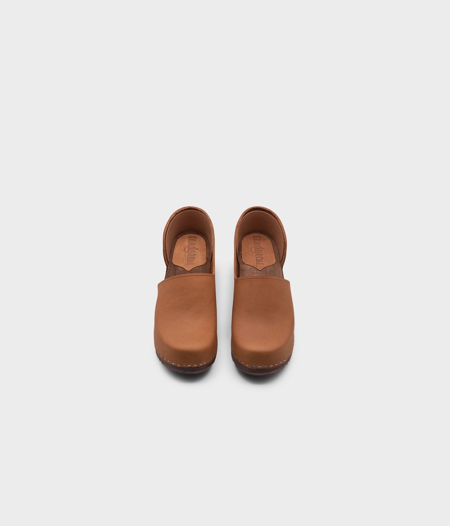 high heeled closed-back clogs in light brown nubuck leather stapled on a dark wooden base