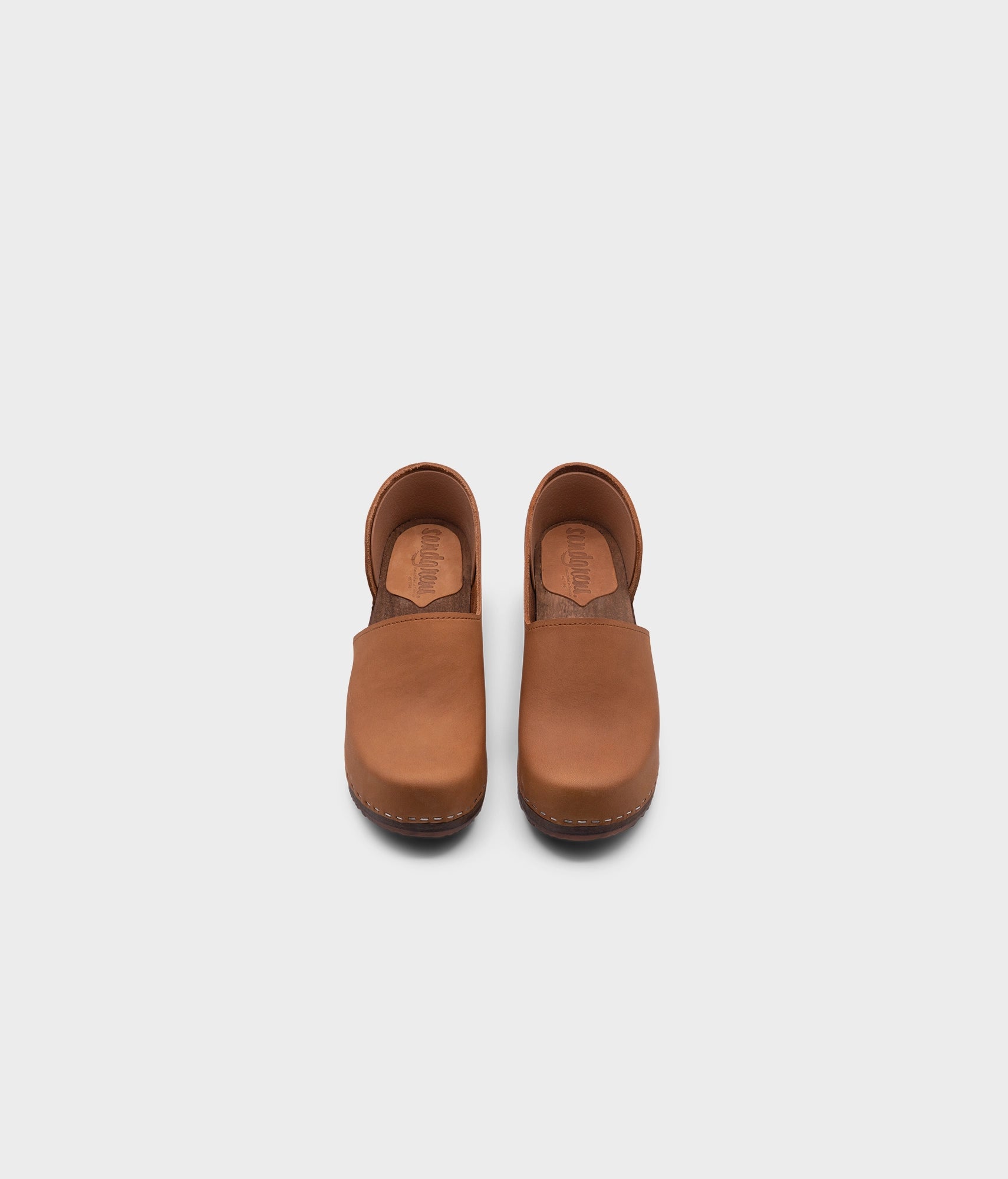 high heeled closed-back clogs in light brown nubuck leather stapled on a dark wooden base