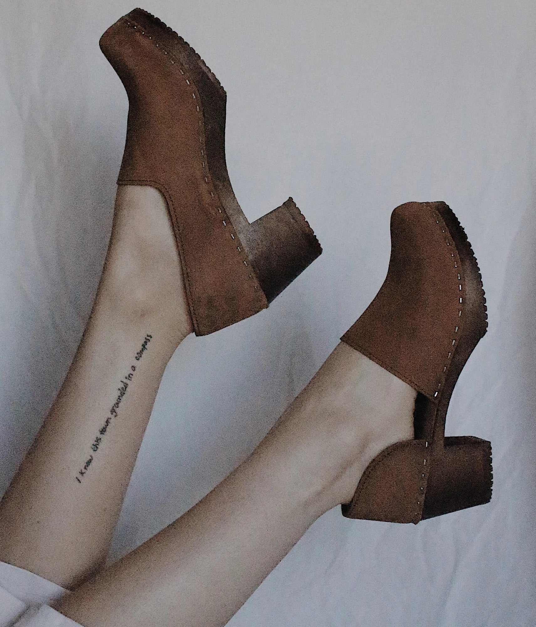 high heeled closed-back clogs in light brown nubuck leather stapled on a dark wooden base