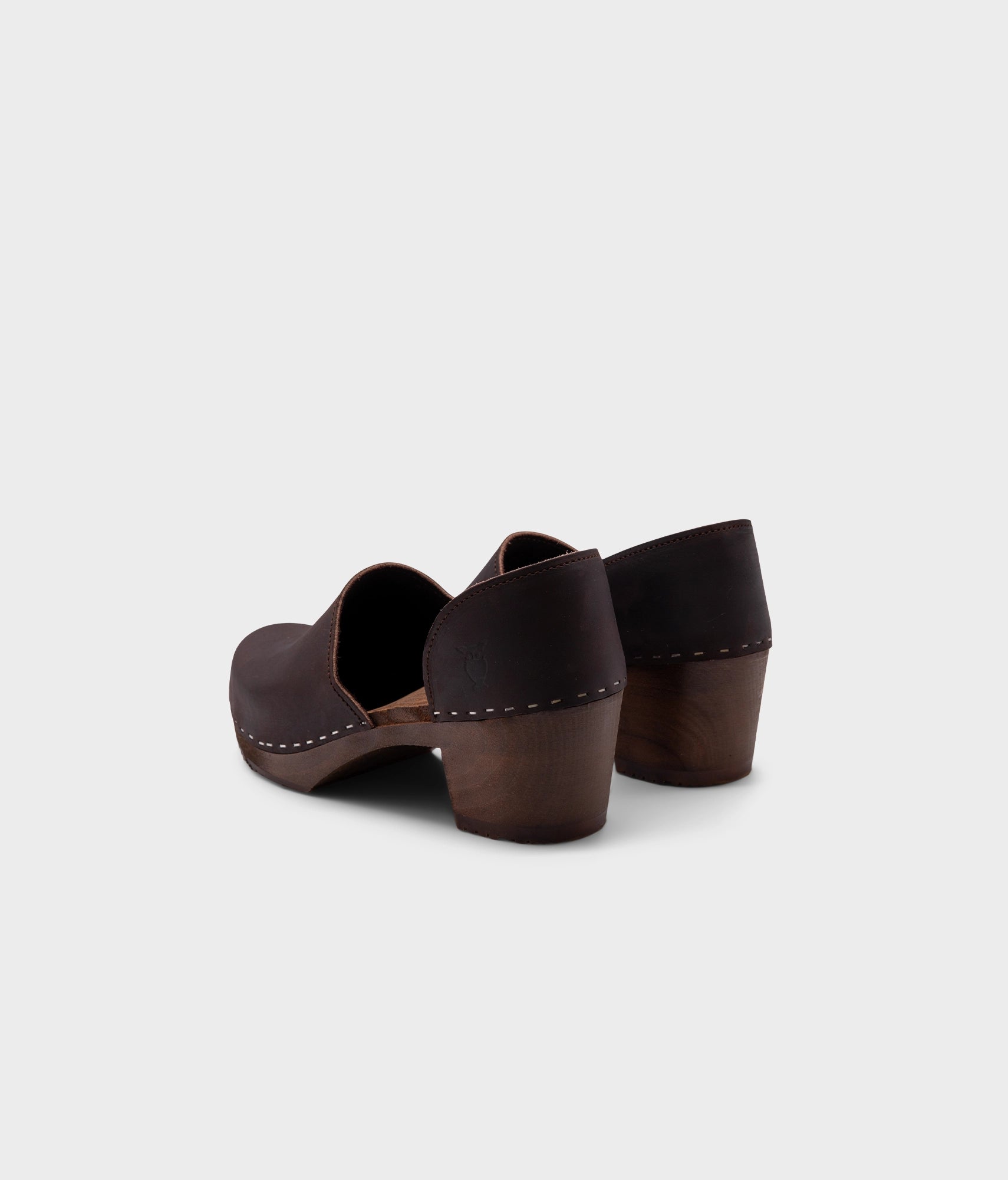 high heeled closed-back clogs in dark brown nubuck leather stapled on a dark wooden base