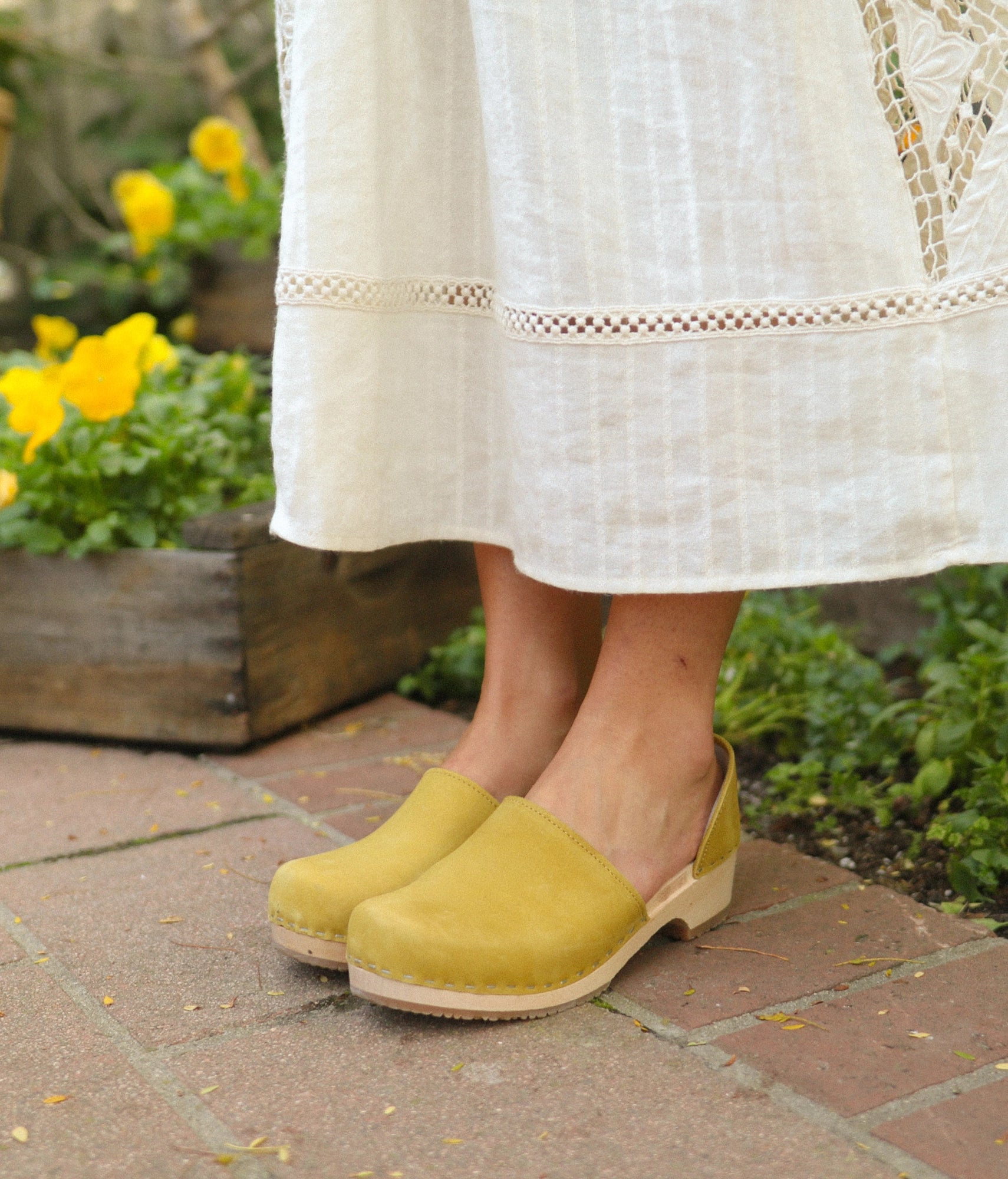 low heeled closed-back clogs in yellow nubuck leather stapled on a light wooden base