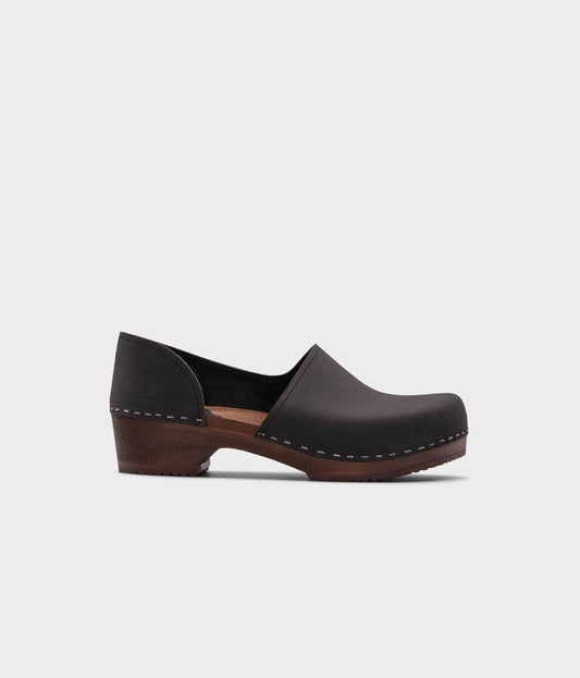 low heeled closed-back clogs in black nubuck leather stapled on a dark wooden base