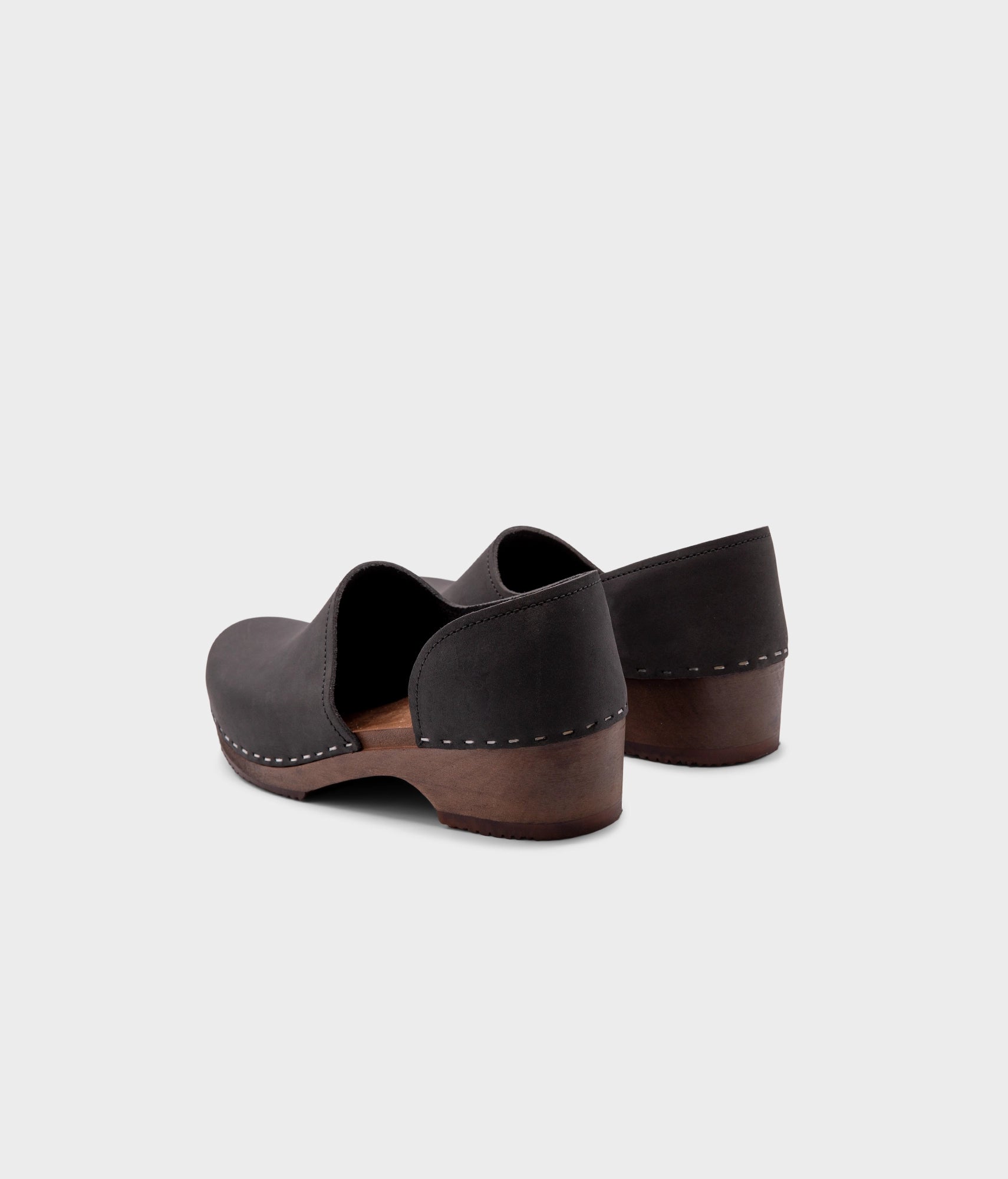 low heeled closed-back clogs in black nubuck leather stapled on a dark wooden base