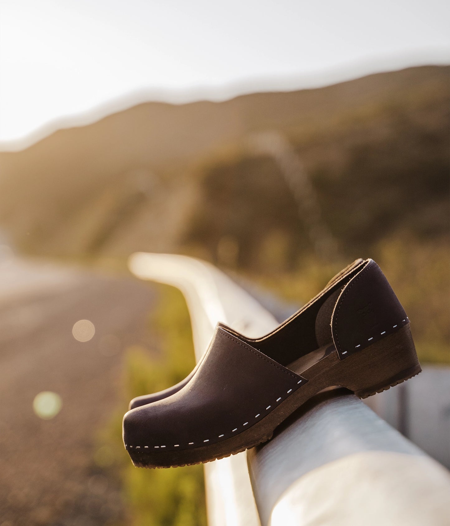 low heeled closed-back clogs in black nubuck leather stapled on a dark wooden base