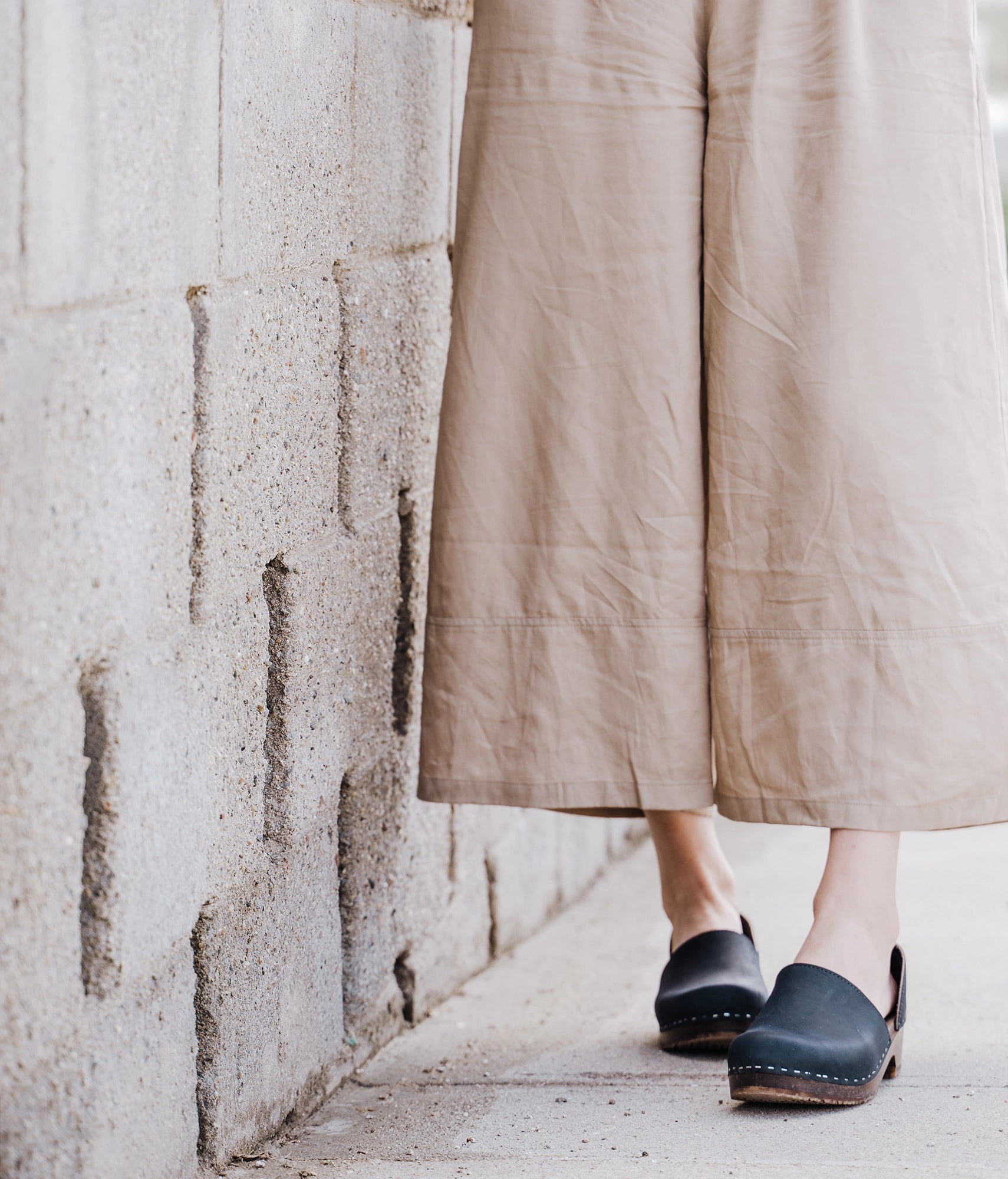 low heeled closed-back clogs in black nubuck leather stapled on a dark wooden base