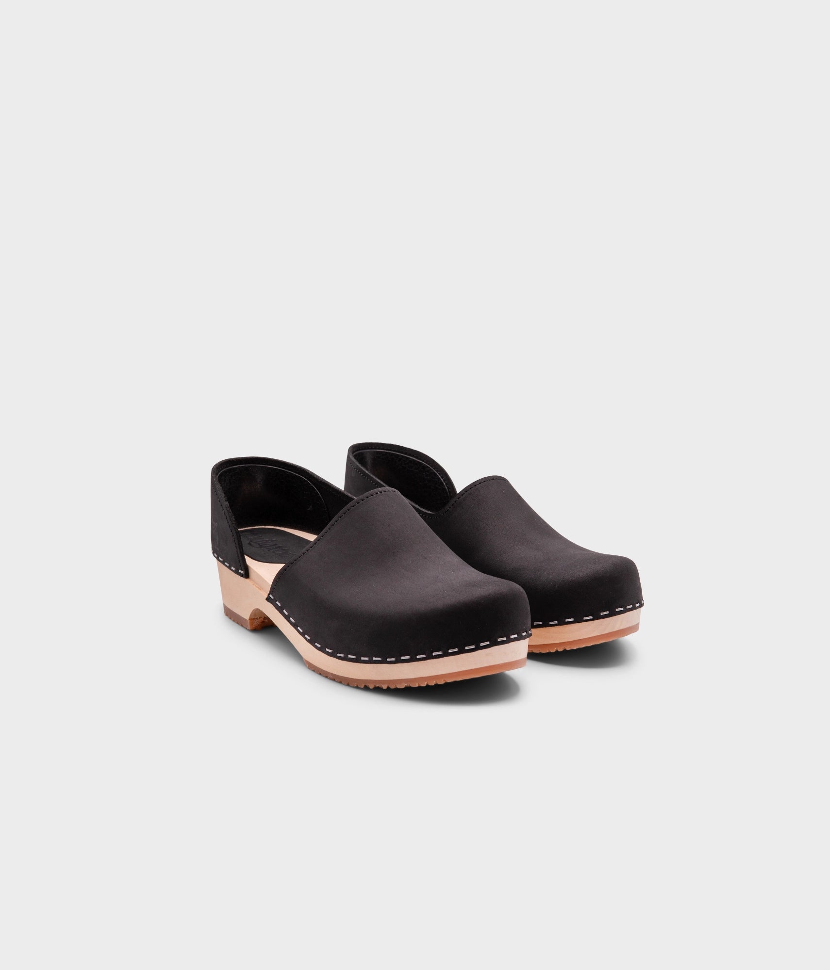 low heeled closed-back clogs in black nubuck leather stapled on a light wooden base