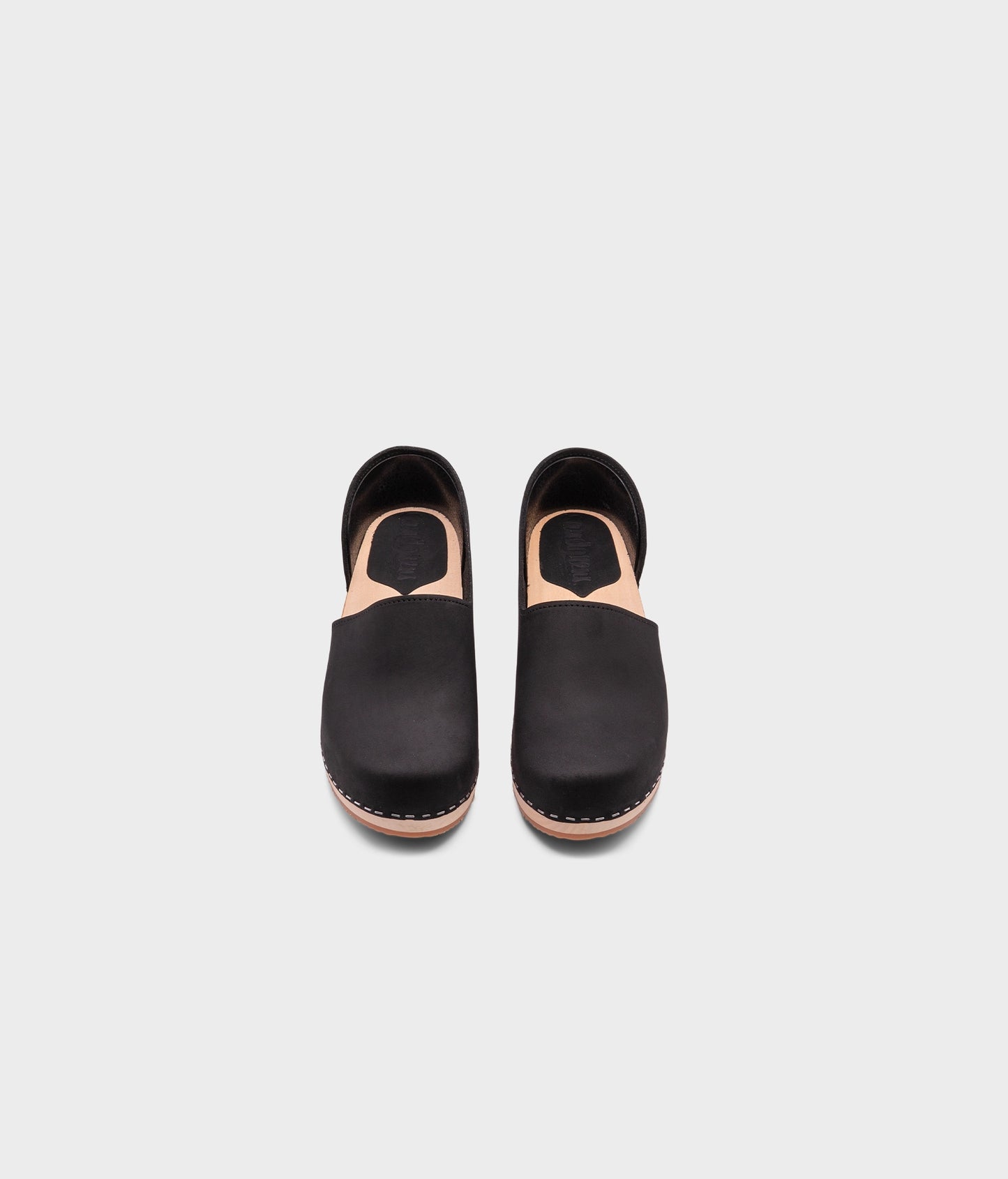 low heeled closed-back clogs in black nubuck leather stapled on a light wooden base