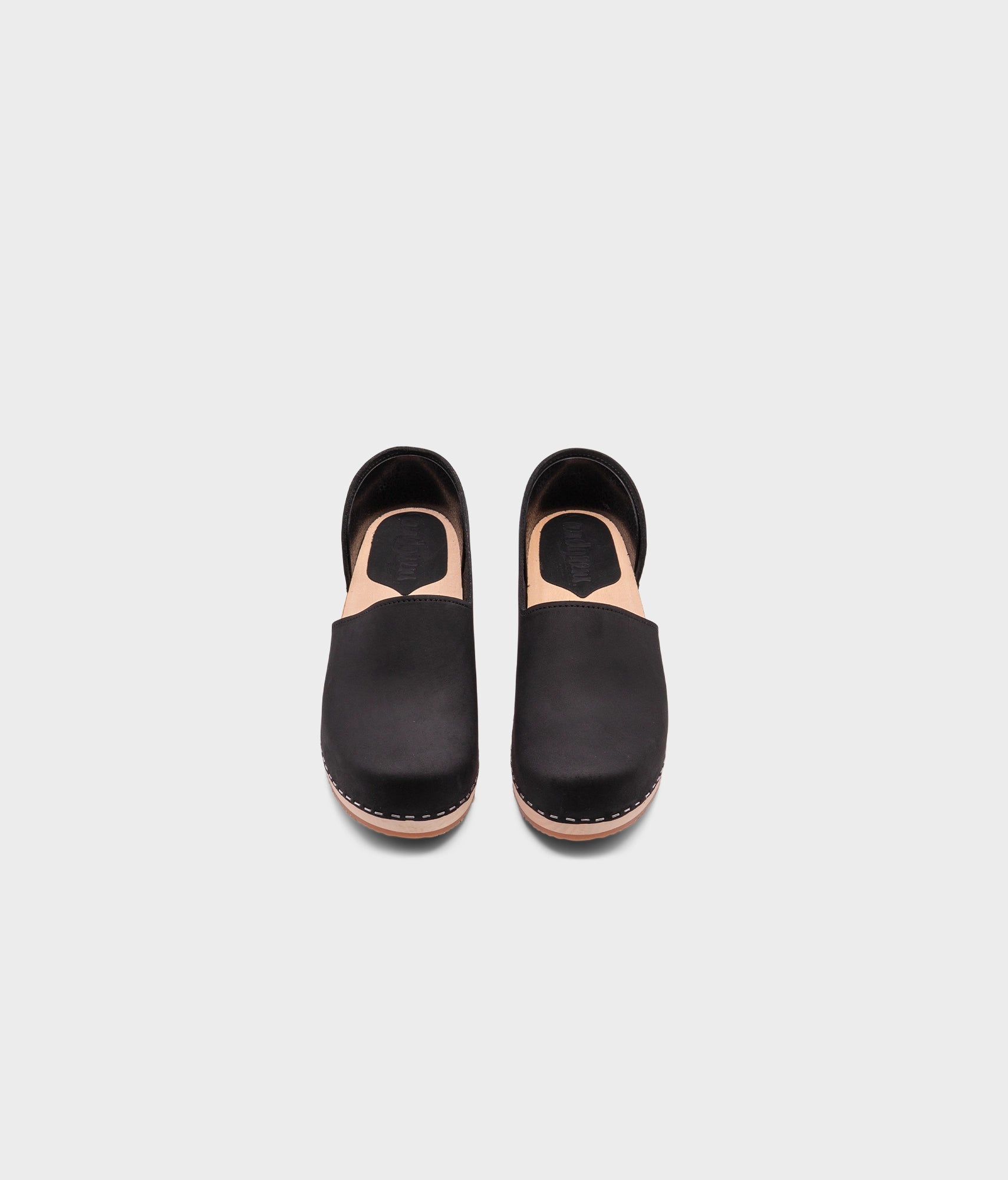 low heeled closed-back clogs in black nubuck leather stapled on a light wooden base