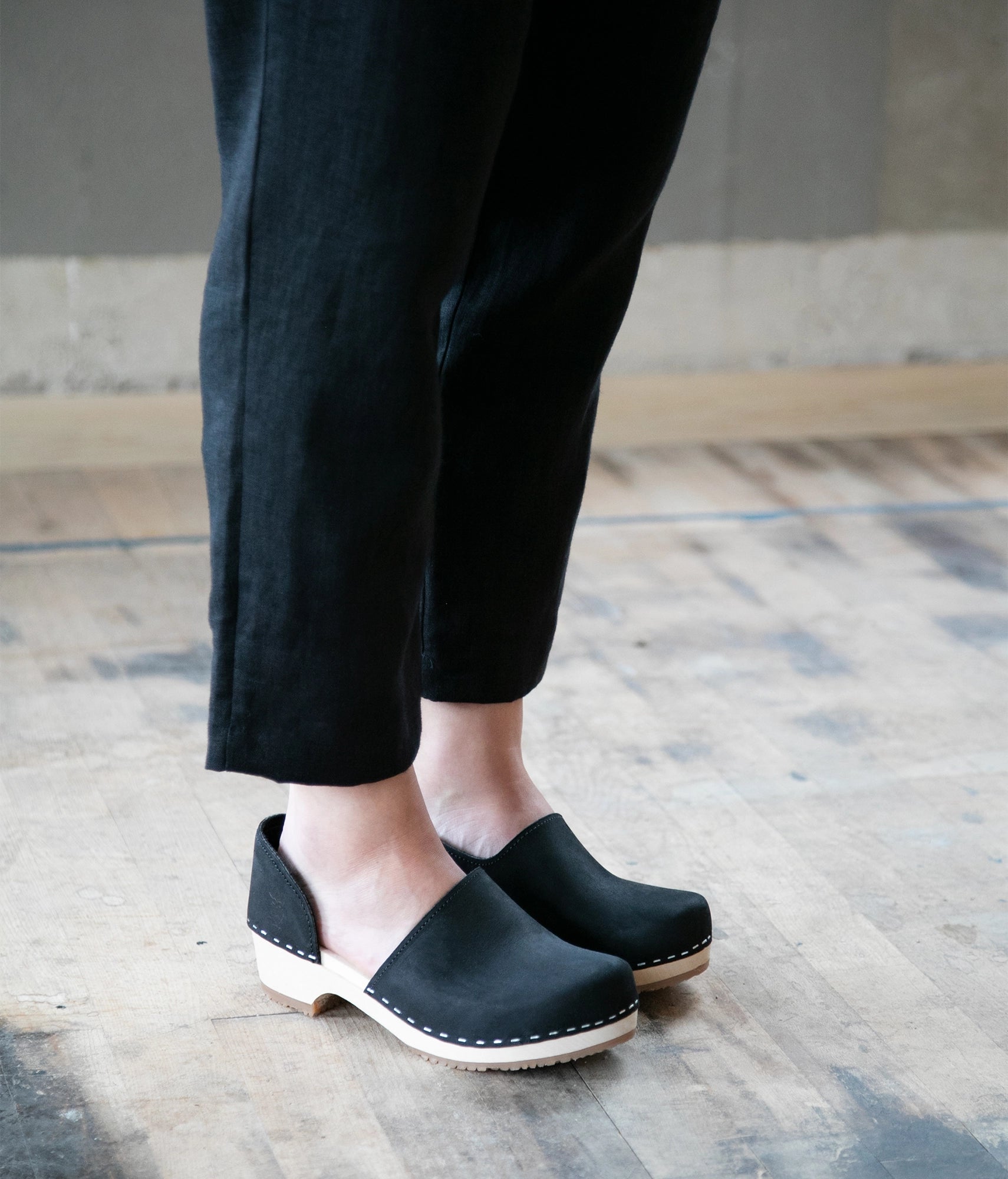 low heeled closed-back clogs in black nubuck leather stapled on a light wooden base