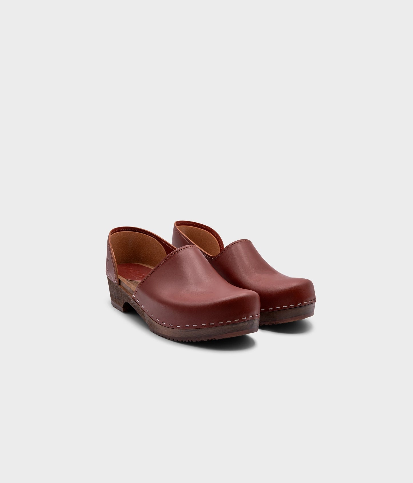 low heeled closed-back clogs in cognac vegetable tanned leather stapled on a dark wooden base