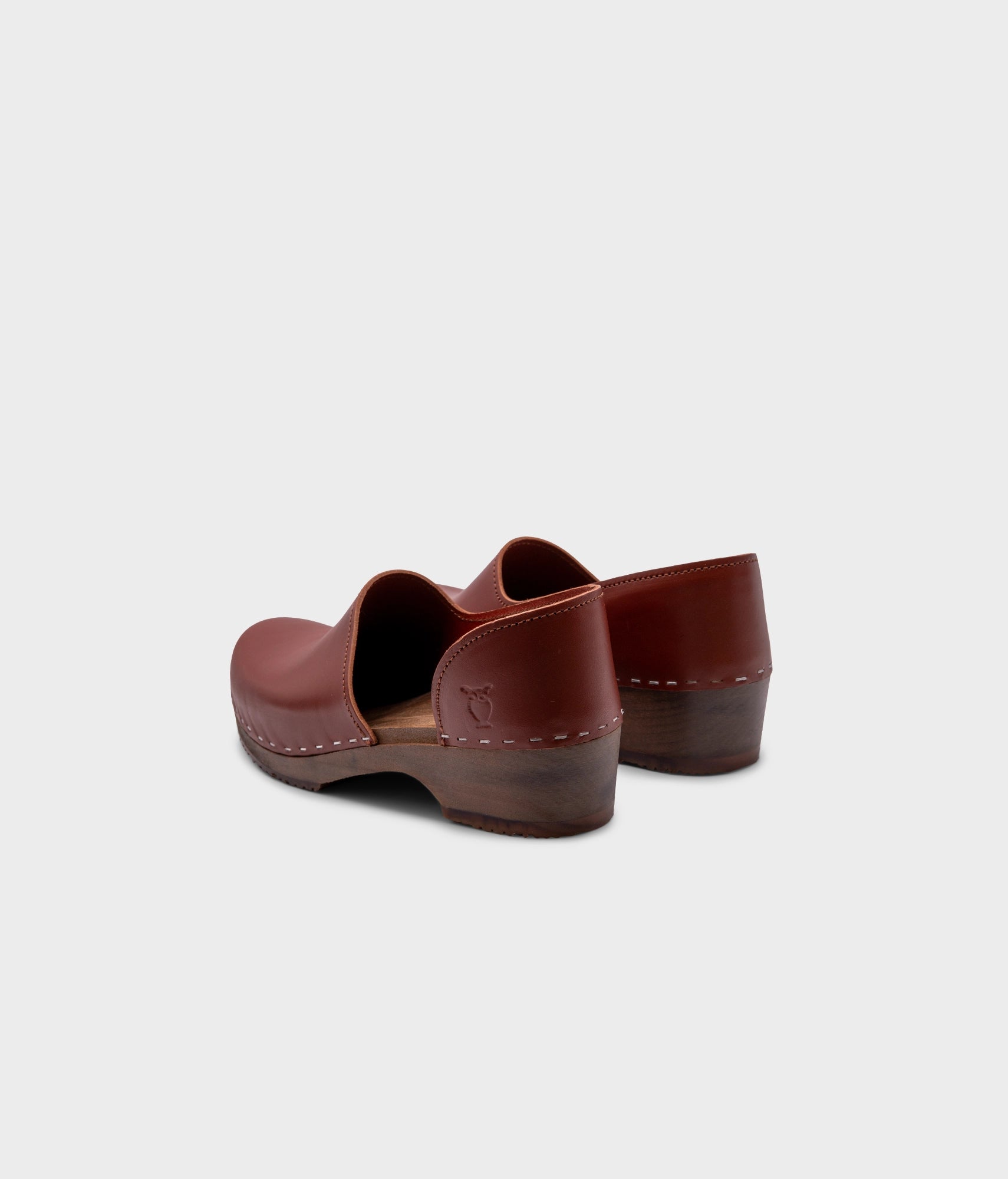 low heeled closed-back clogs in cognac vegetable tanned leather stapled on a dark wooden base