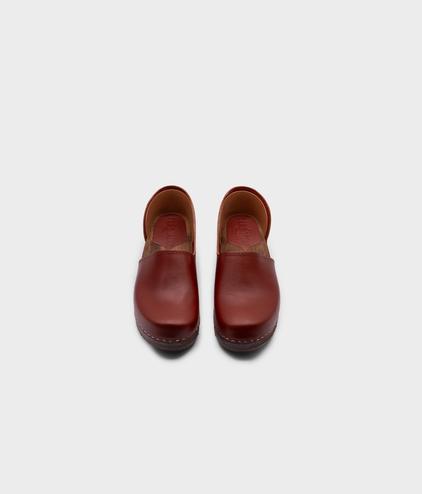 low heeled closed-back clogs in cognac vegetable tanned leather stapled on a dark wooden base