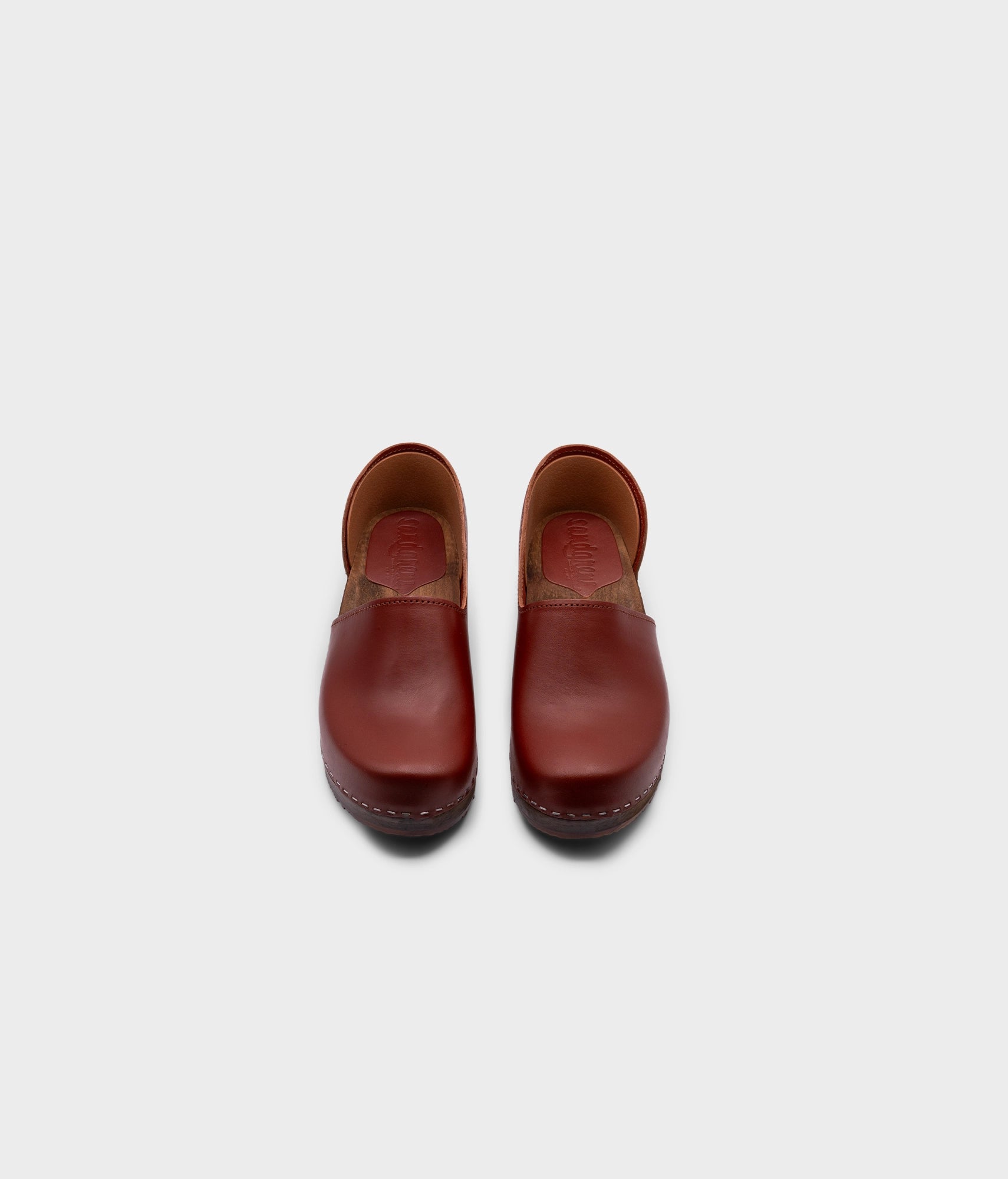 low heeled closed-back clogs in cognac vegetable tanned leather stapled on a dark wooden base