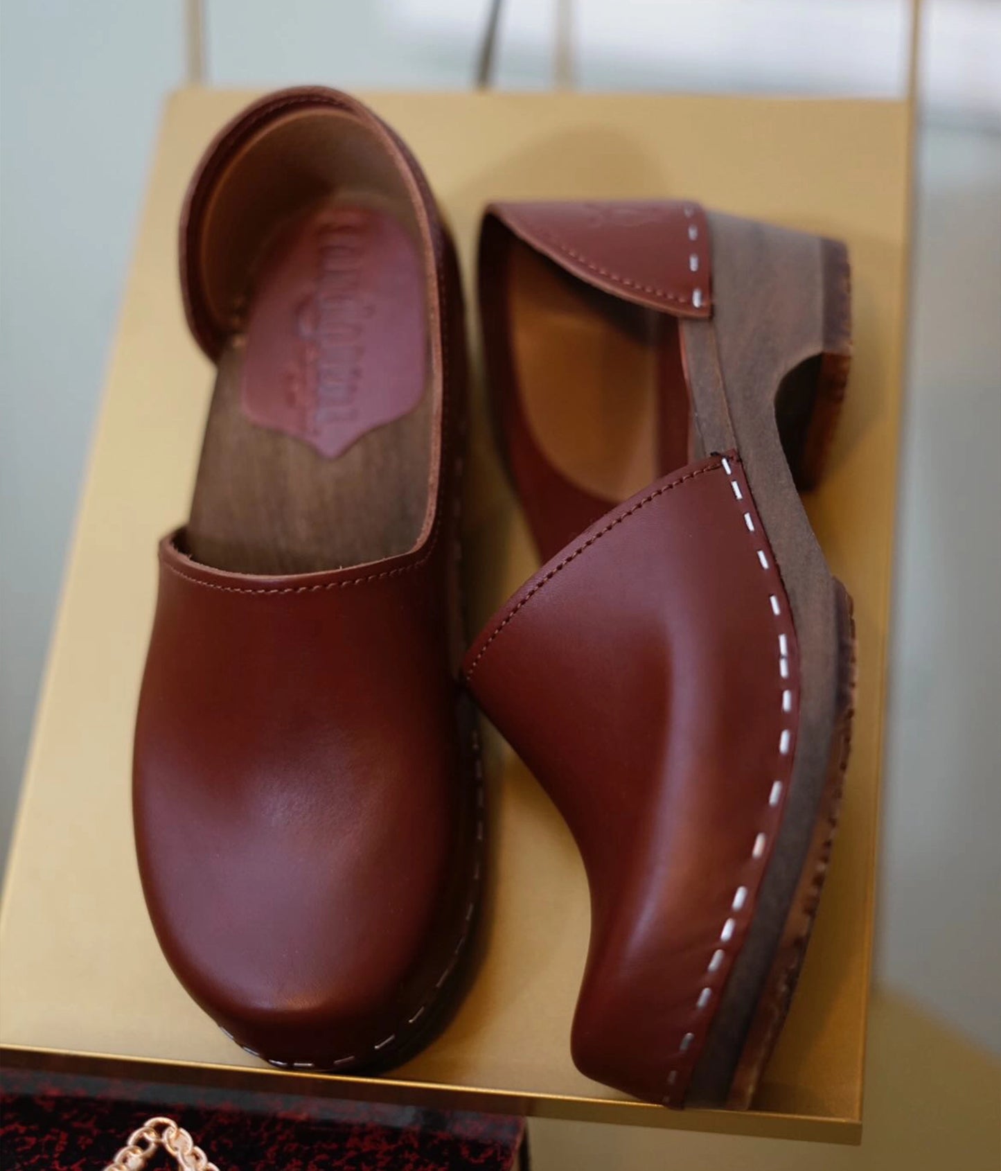 low heeled closed-back clogs in cognac vegetable tanned leather stapled on a dark wooden base