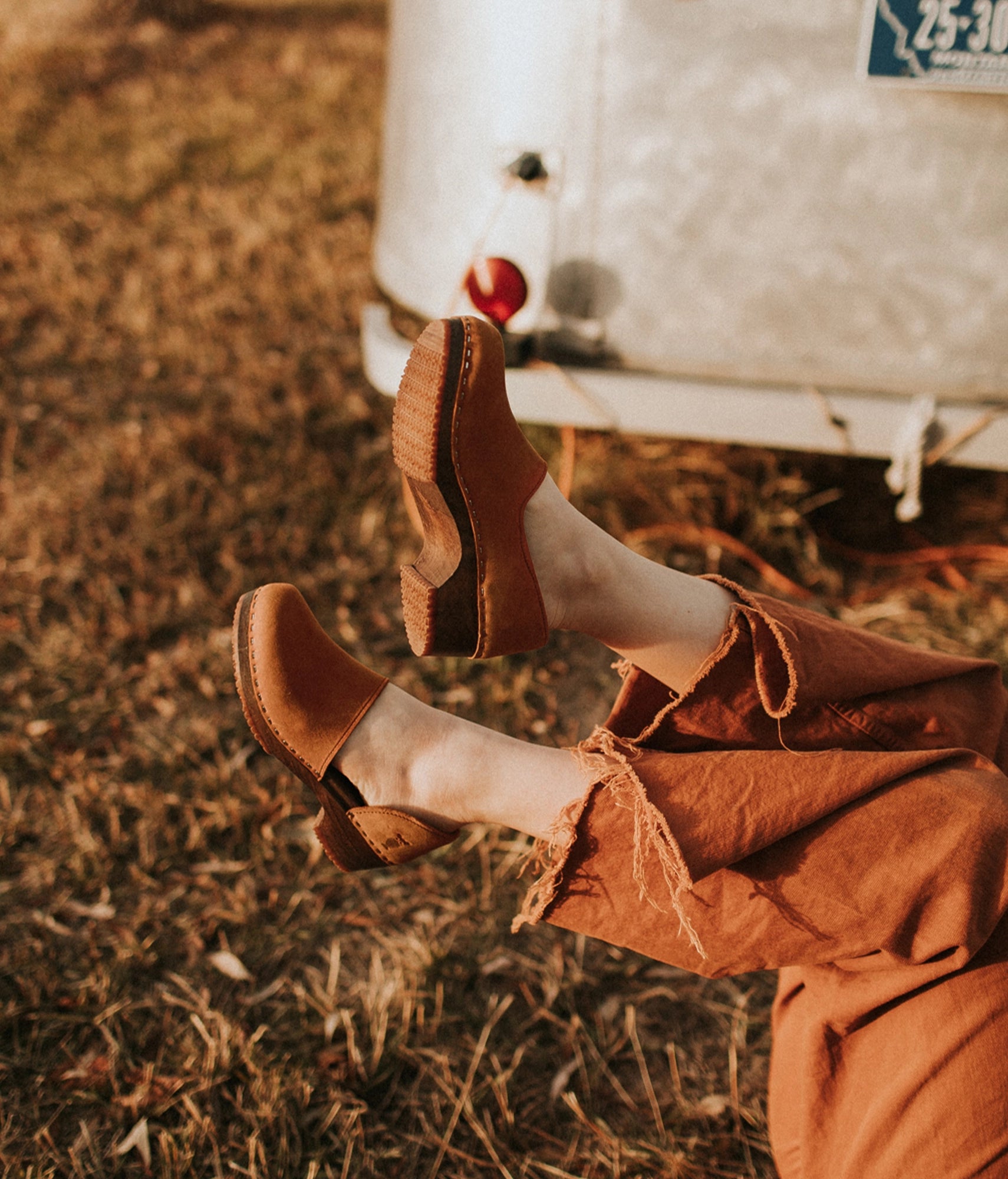 low heeled closed-back clogs in light brown nubuck leather stapled on a dark wooden base