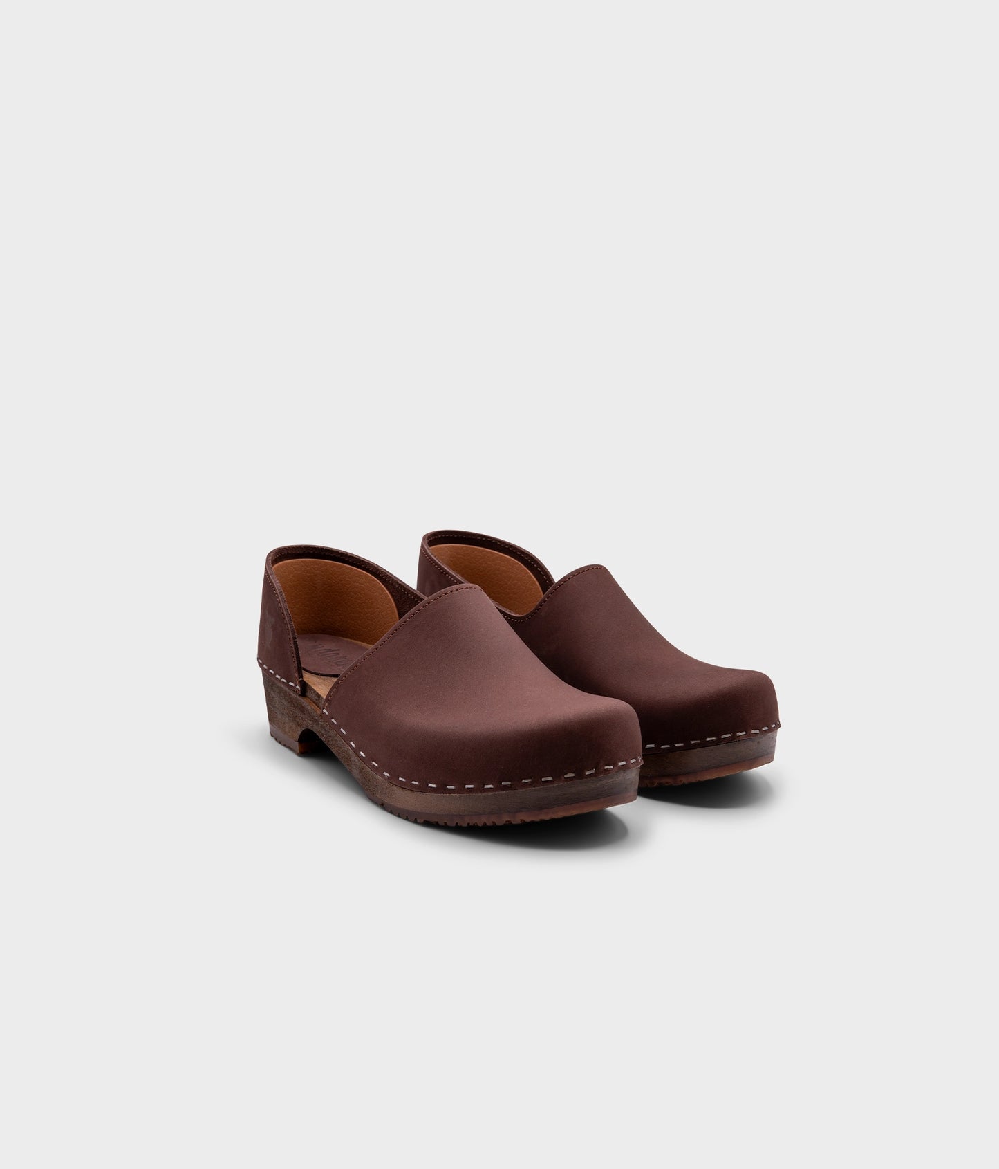 low heeled closed-back clogs in dark brown nubuck leather stapled on a dark wooden base