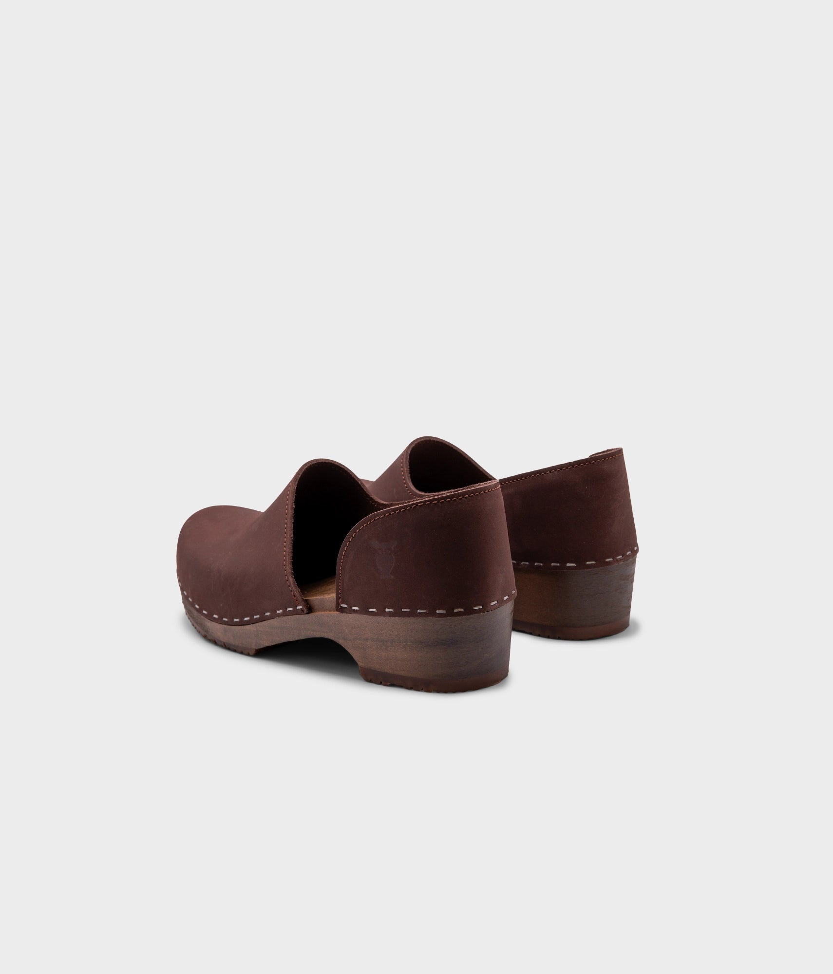 low heeled closed-back clogs in dark brown nubuck leather stapled on a dark wooden base