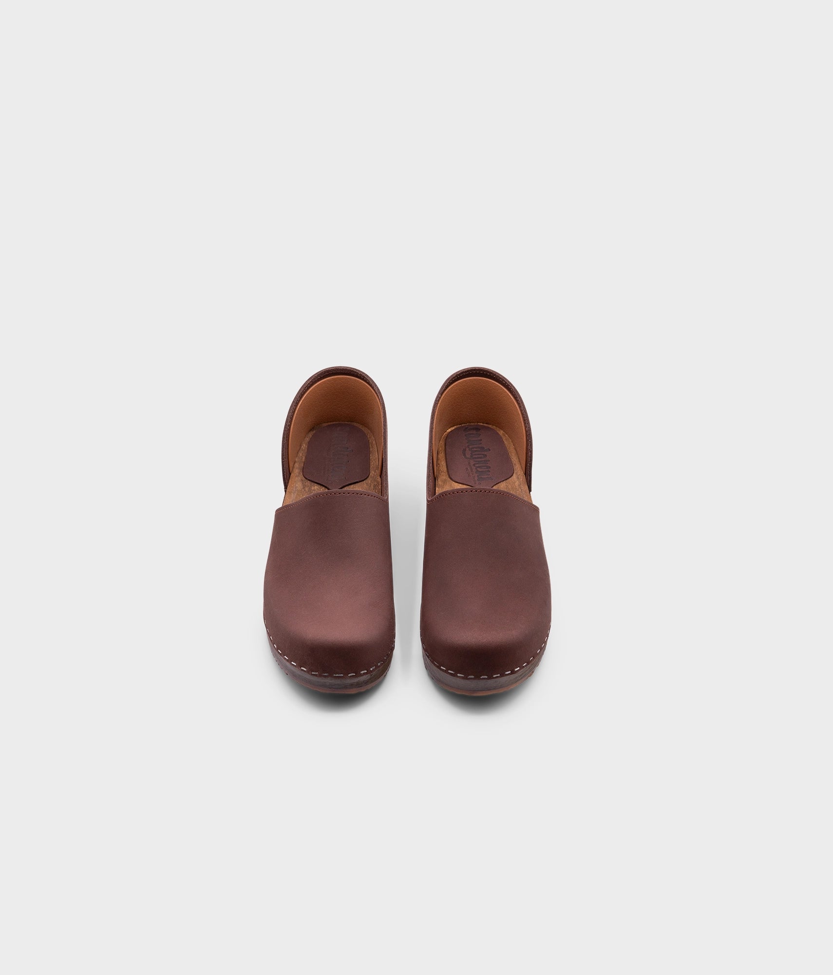 low heeled closed-back clogs in dark brown nubuck leather stapled on a dark wooden base
