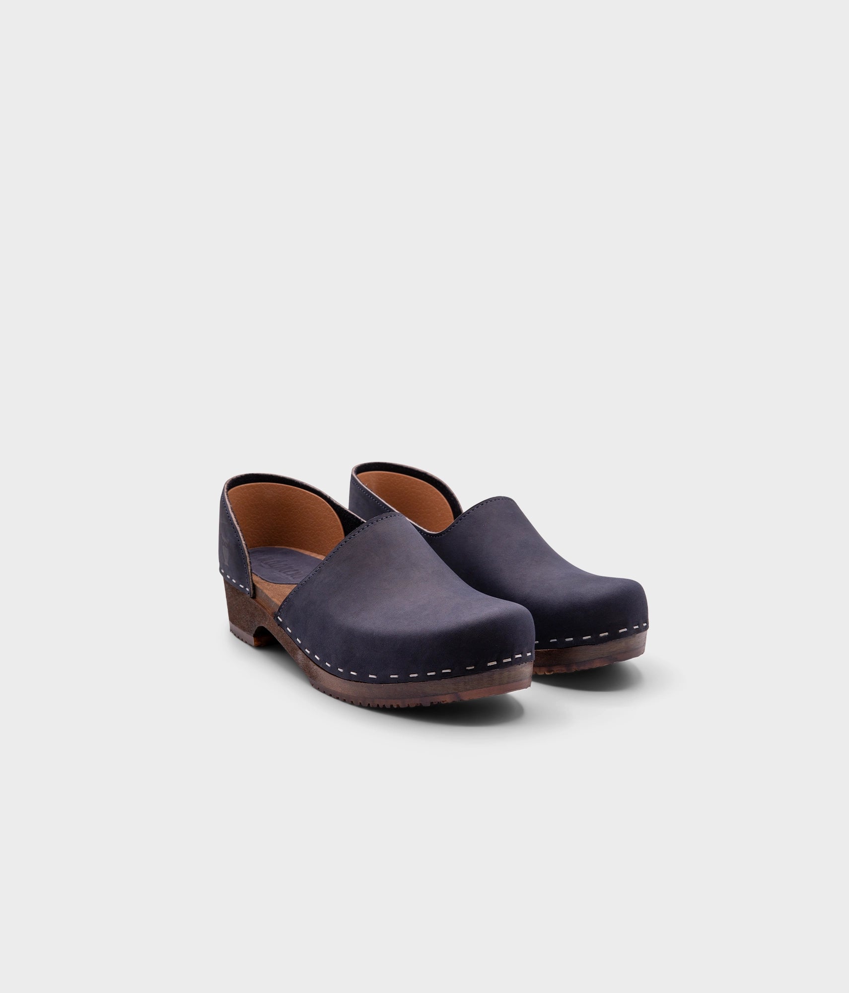 low heeled closed-back clogs in navy blue nubuck leather stapled on a dark wooden base