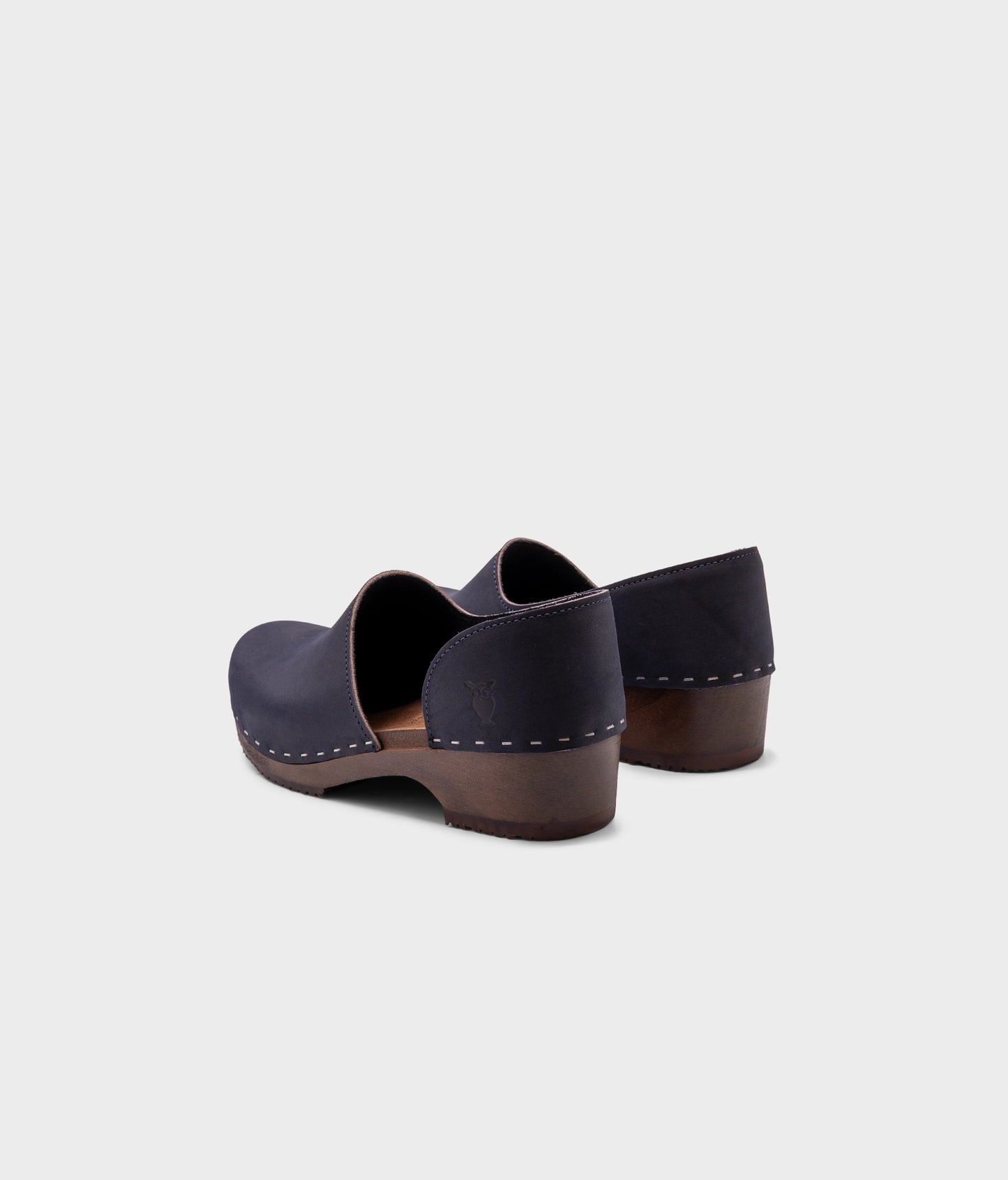 low heeled closed-back clogs in navy blue nubuck leather stapled on a dark wooden base