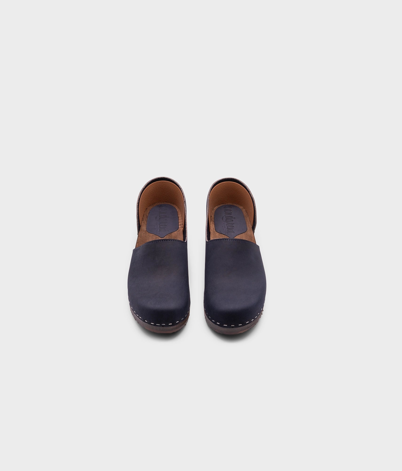 low heeled closed-back clogs in navy blue nubuck leather stapled on a dark wooden base