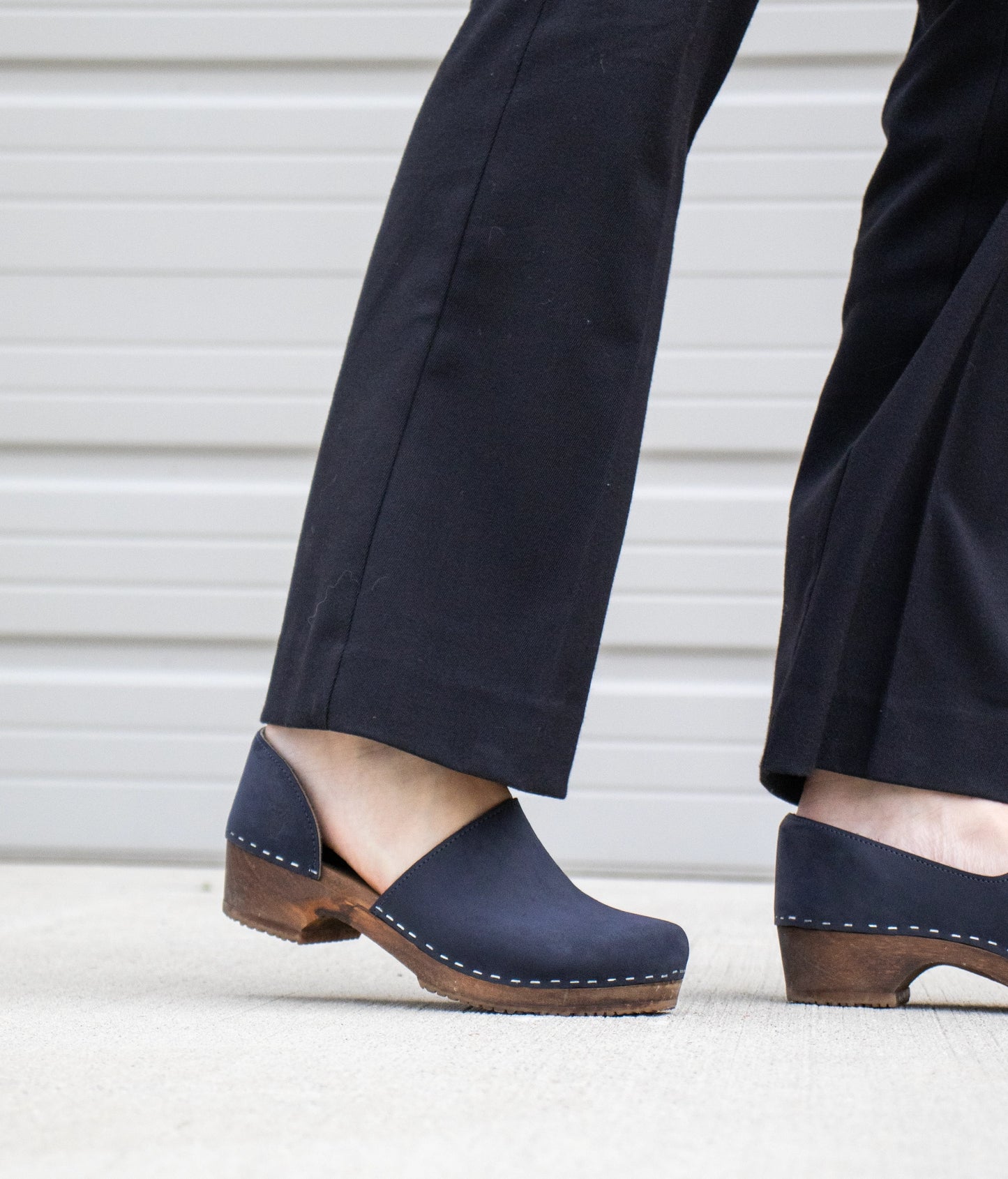 low heeled closed-back clogs in navy blue nubuck leather stapled on a dark wooden base