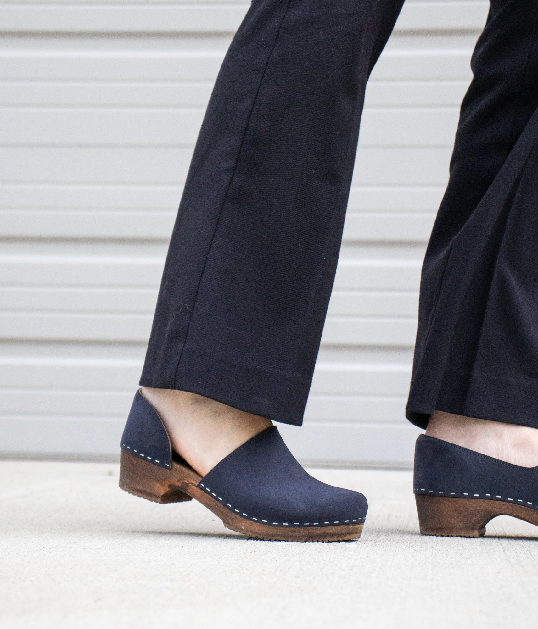 low heeled closed-back clogs in navy blue nubuck leather stapled on a dark wooden base
