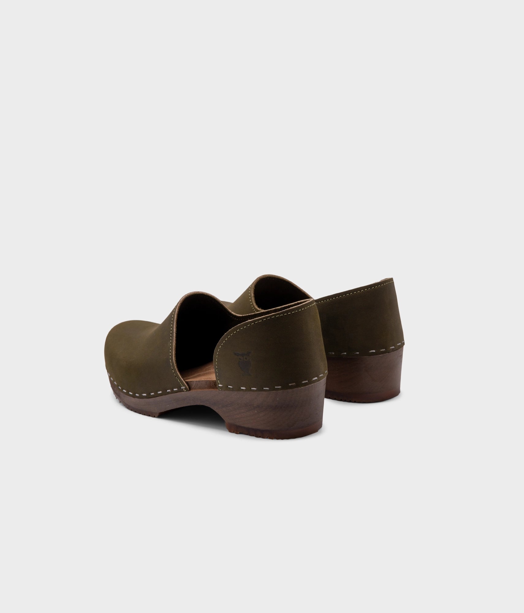 low heeled closed-back clogs in olive green nubuck leather stapled on a dark wooden base