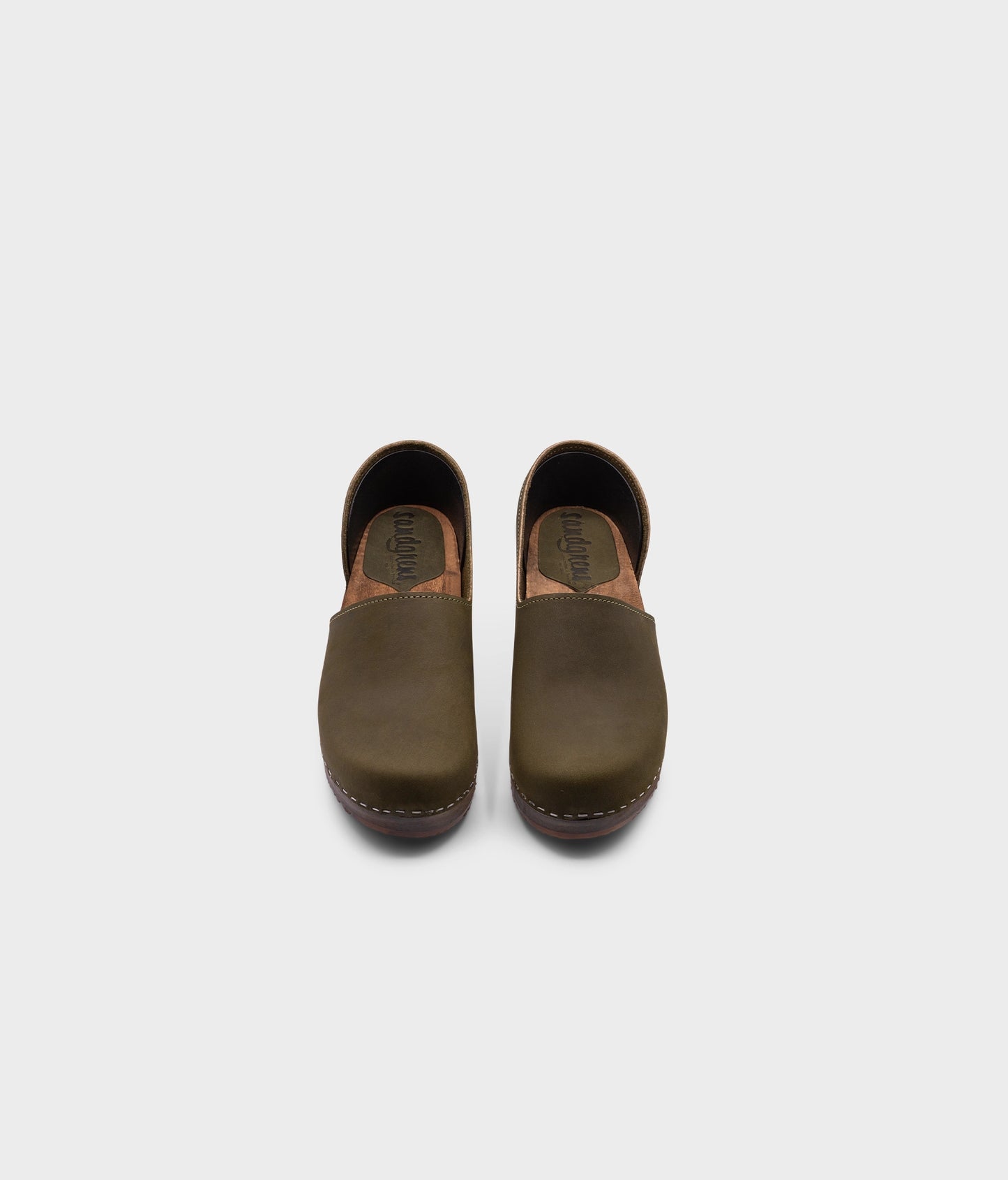 low heeled closed-back clogs in olive green nubuck leather stapled on a dark wooden base
