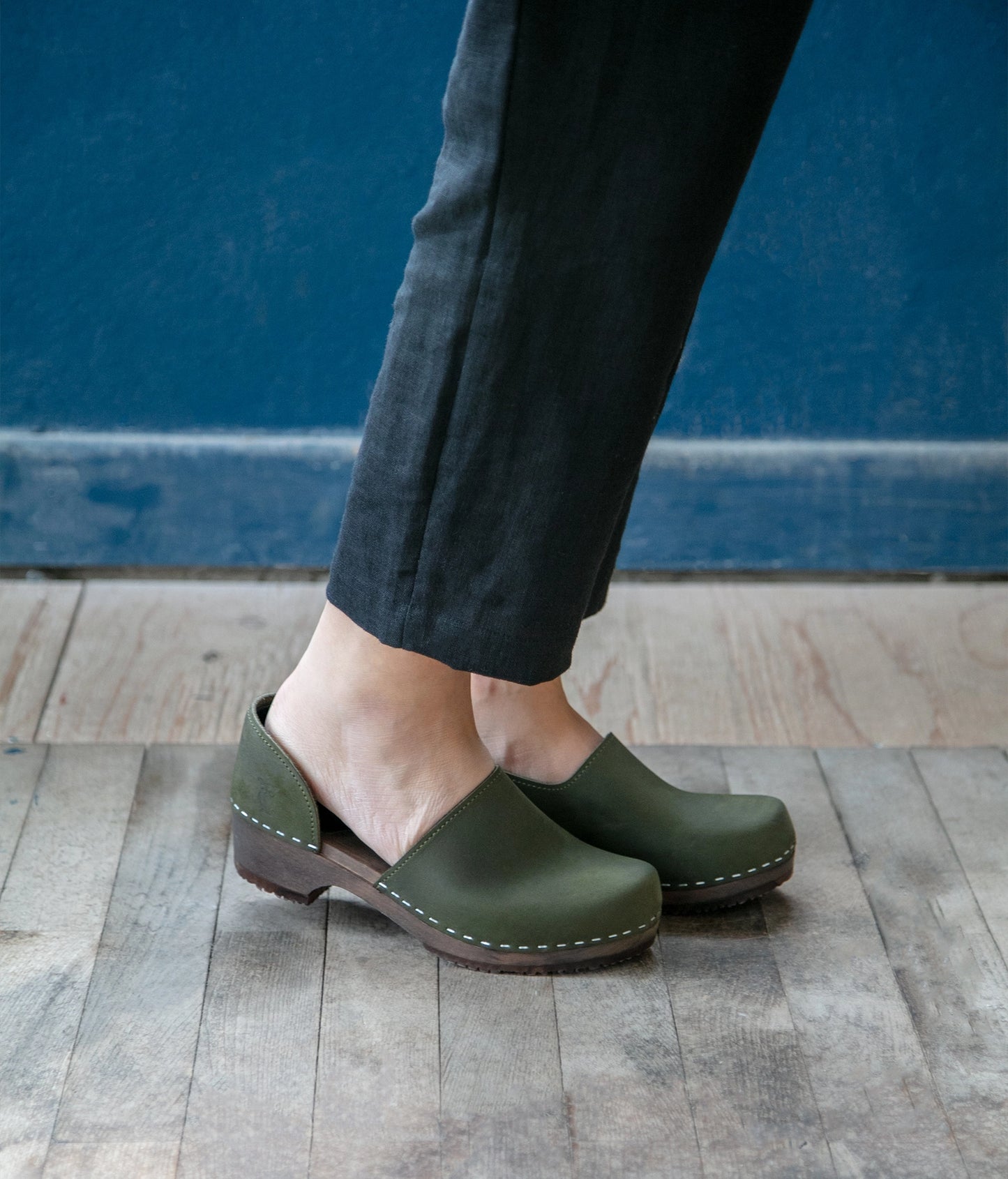 low heeled closed-back clogs in olive green nubuck leather stapled on a dark wooden base
