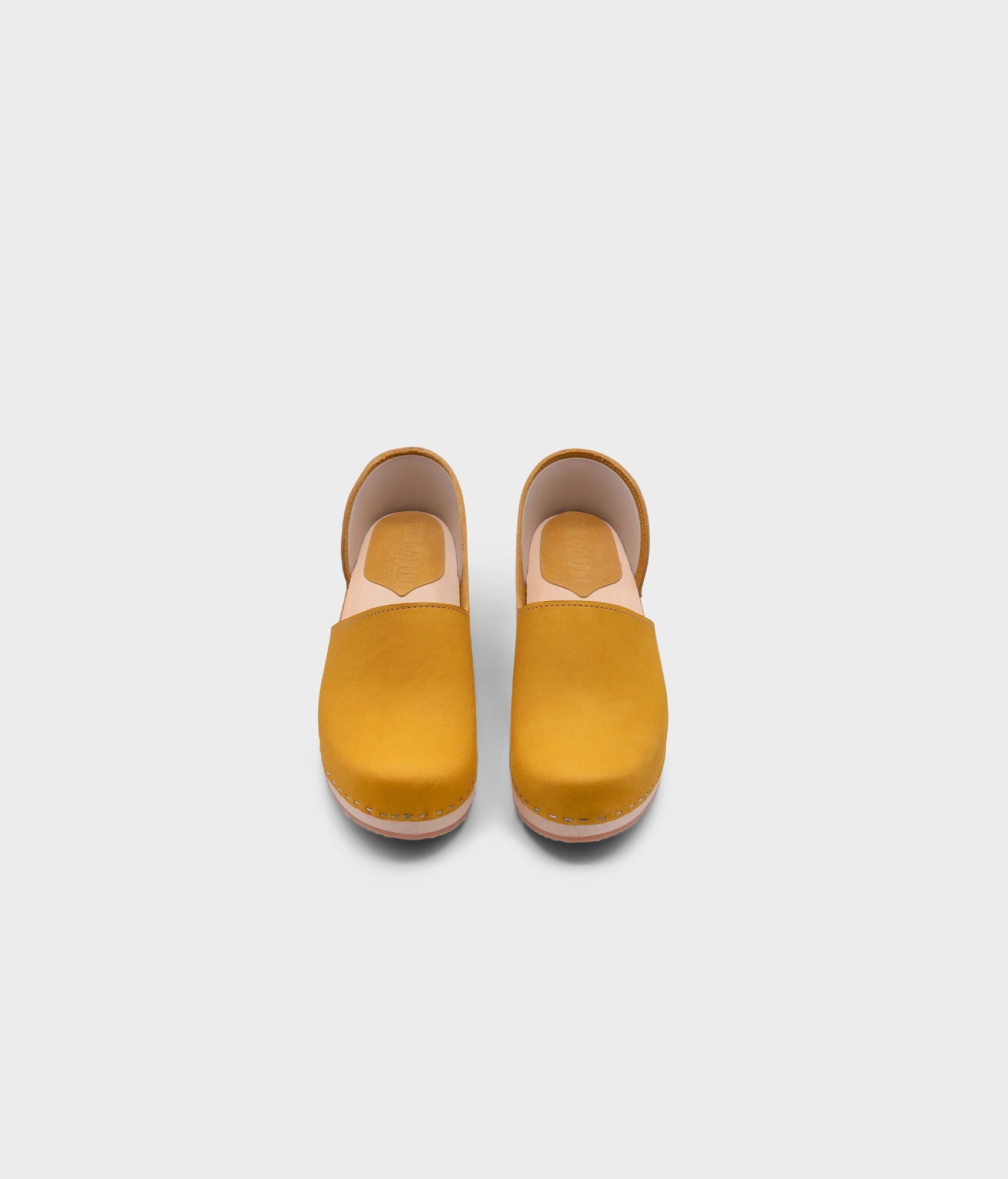 low heeled closed-back clogs in yellow nubuck leather stapled on a light wooden base