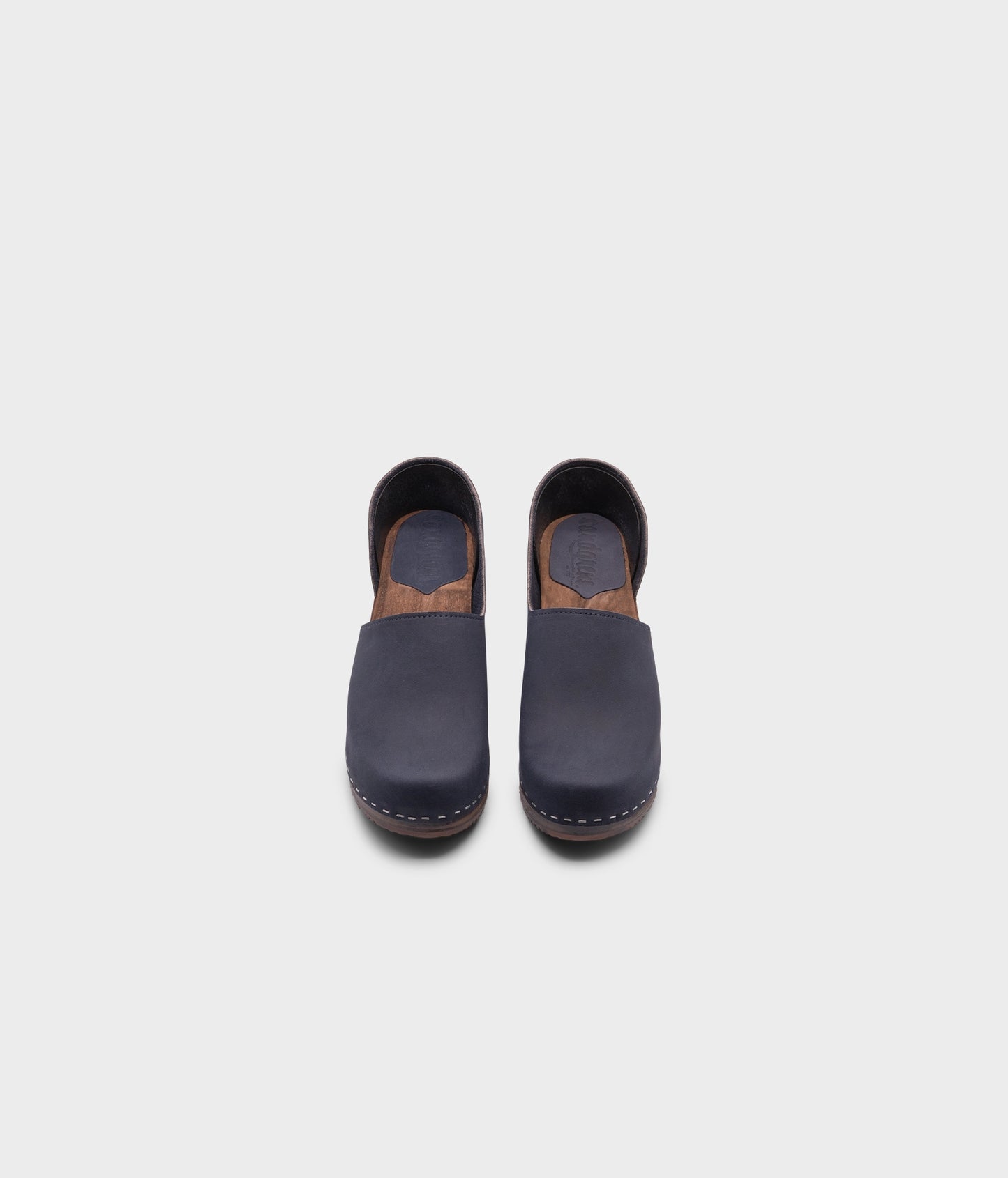 high heeled closed-back clogs in navy blue nubuck leather stapled on a dark wooden base