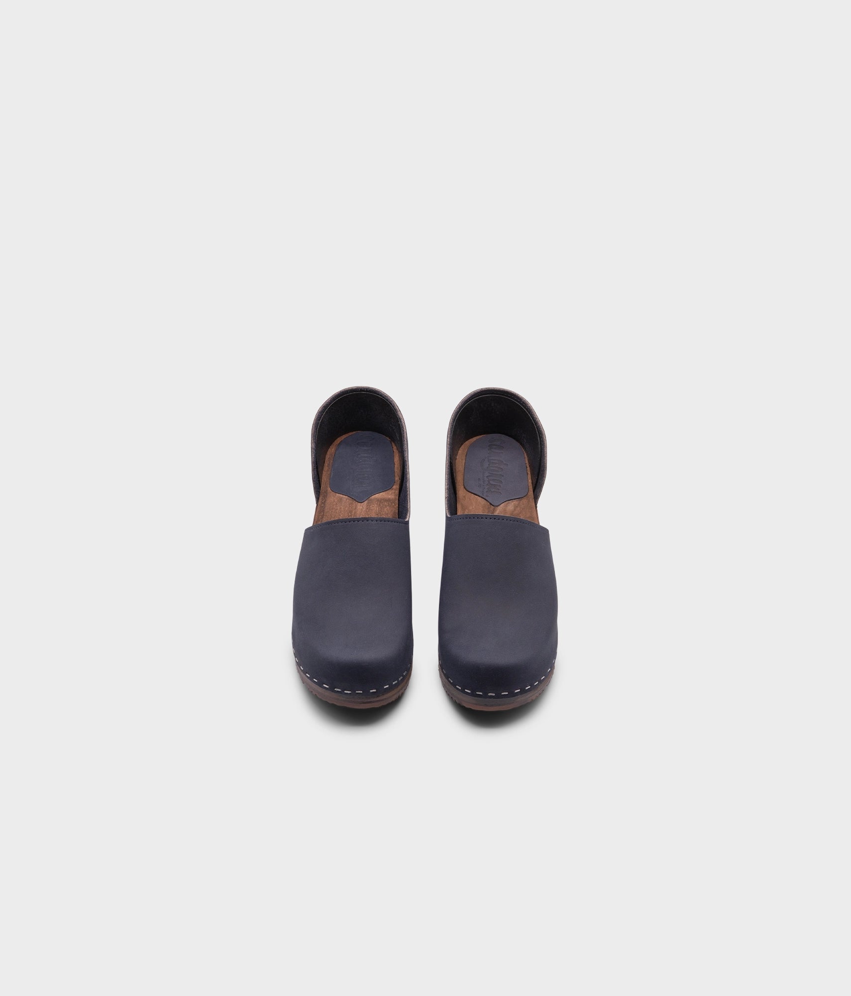 high heeled closed-back clogs in navy blue nubuck leather stapled on a dark wooden base