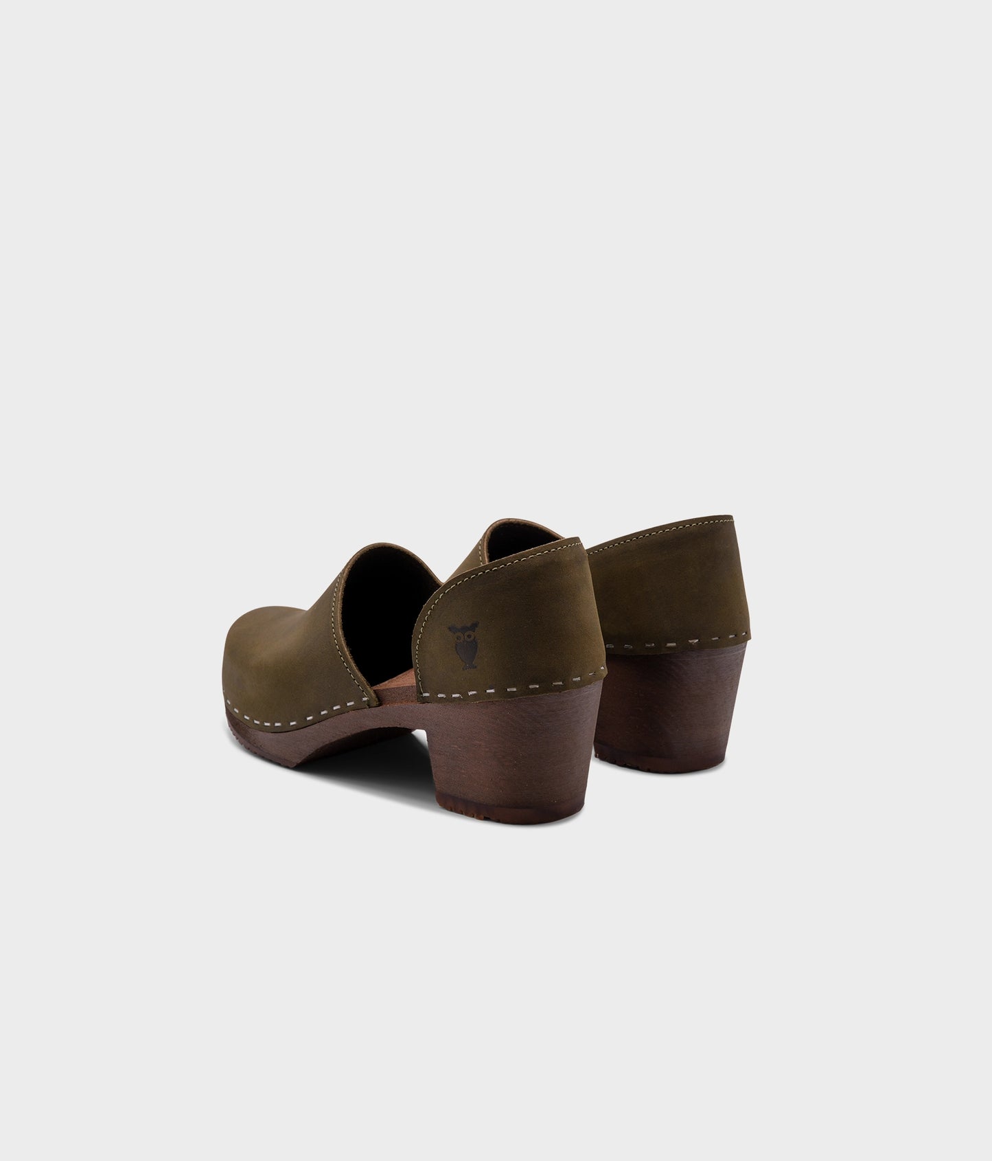 high heeled closed-back clogs in olive green nubuck leather stapled on a dark wooden base