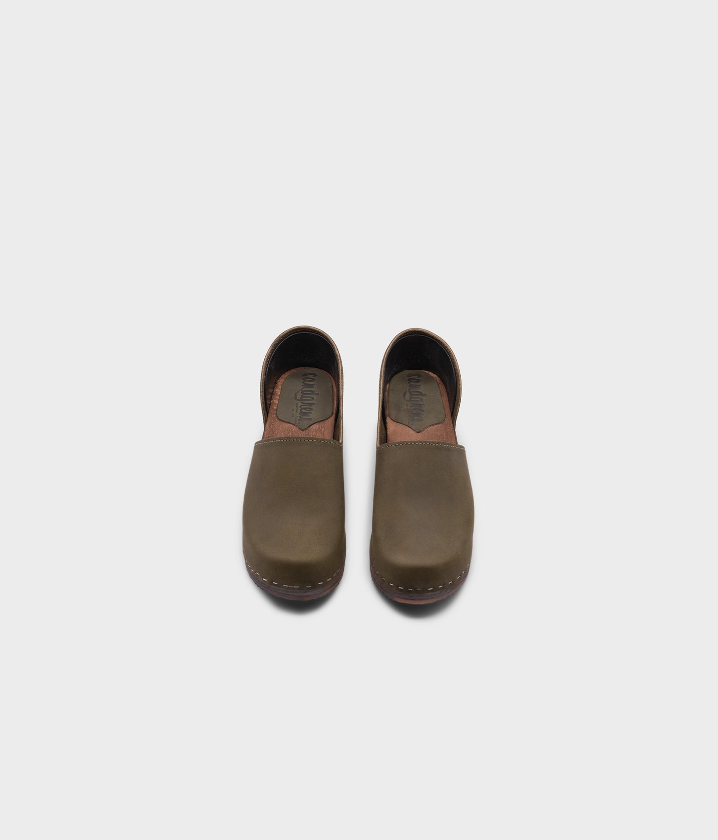 high heeled closed-back clogs in olive green nubuck leather stapled on a dark wooden base