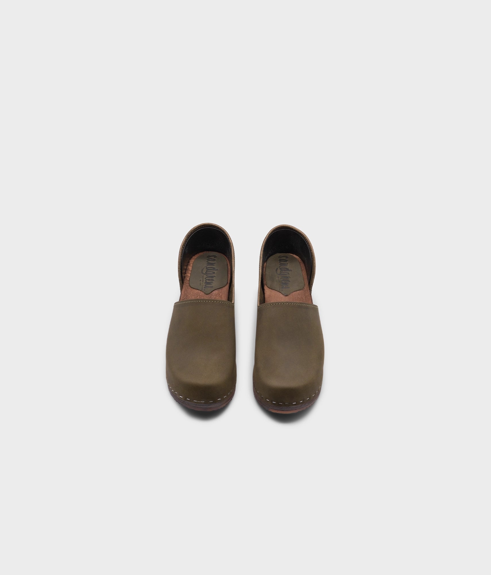 high heeled closed-back clogs in olive green nubuck leather stapled on a dark wooden base