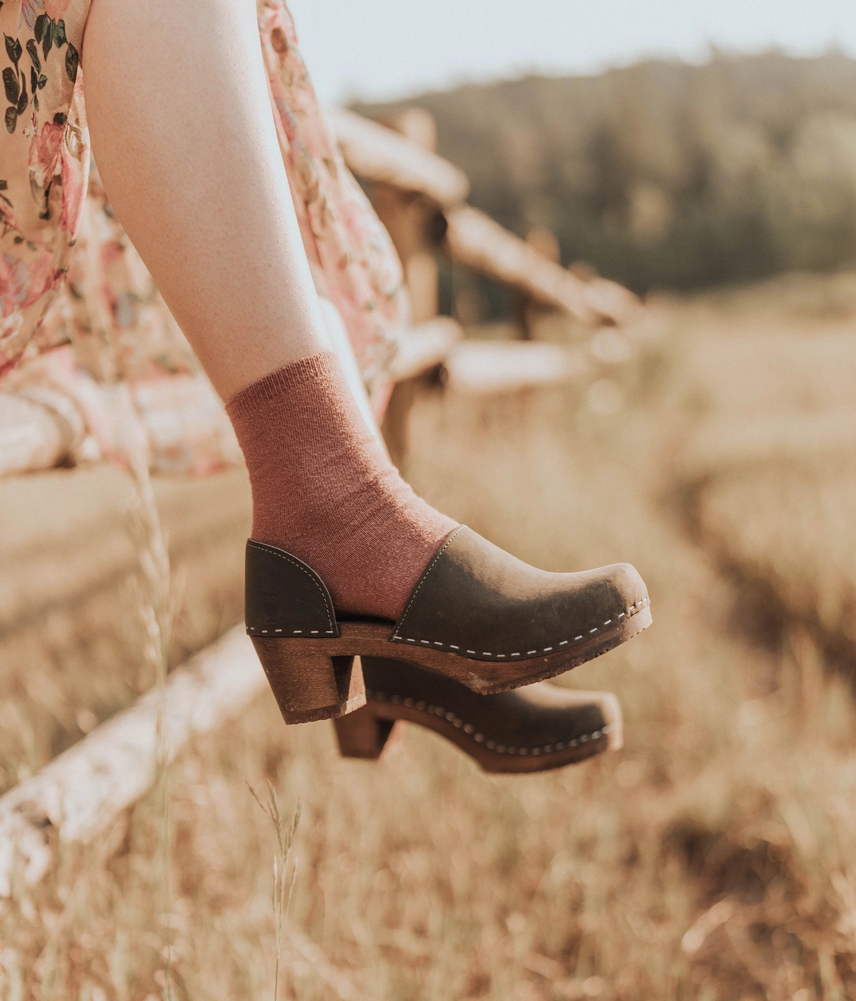 high heeled closed-back clogs in olive green nubuck leather stapled on a dark wooden base