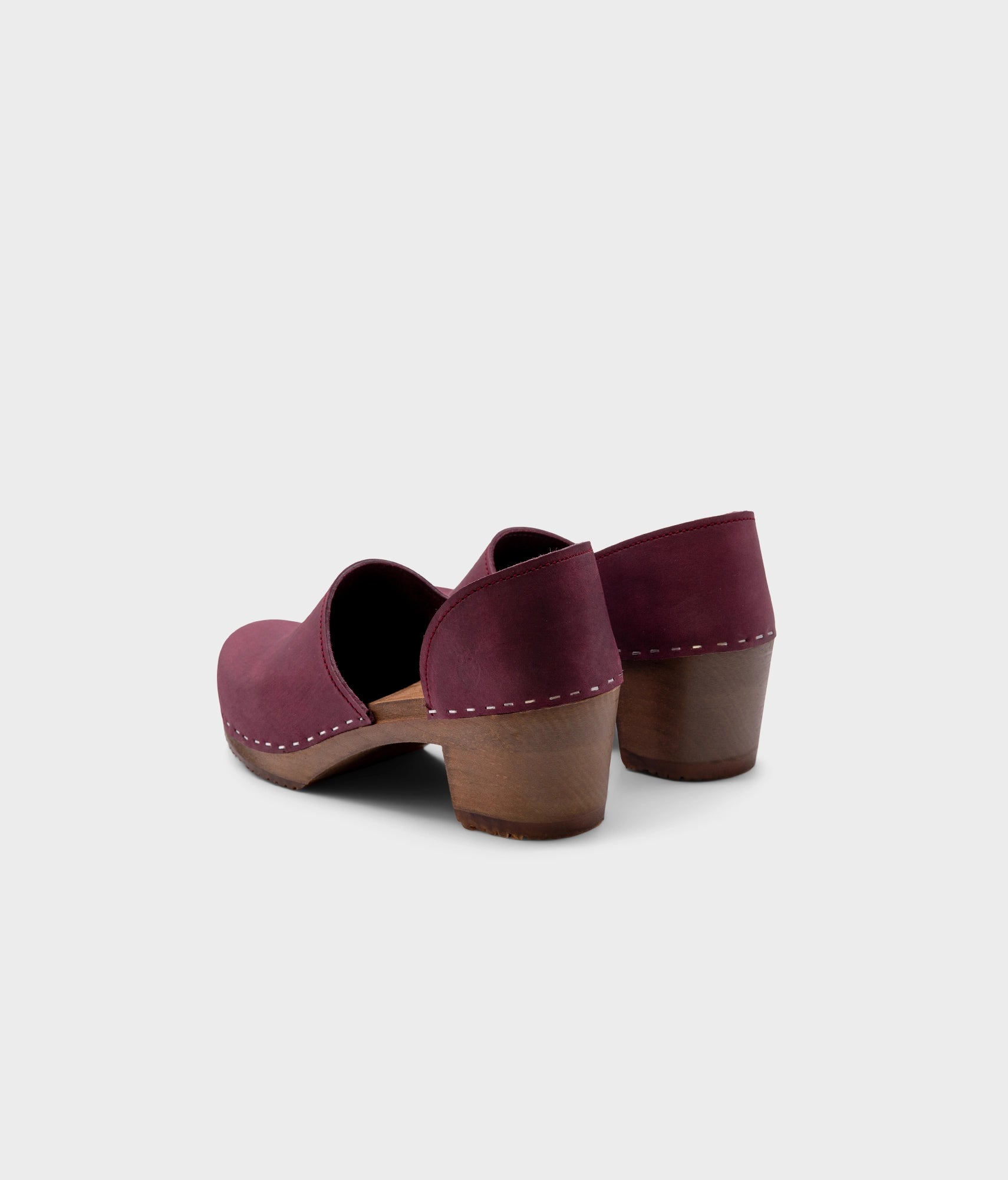 high heeled closed-back clogs in purple plum nubuck leather stapled on a dark wooden base