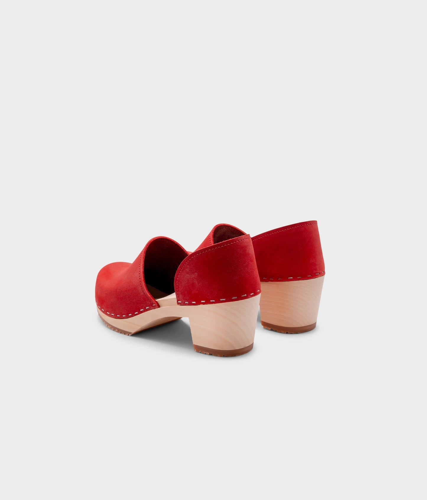 high heeled closed-back clogs in red nubuck leather stapled on a light wooden base