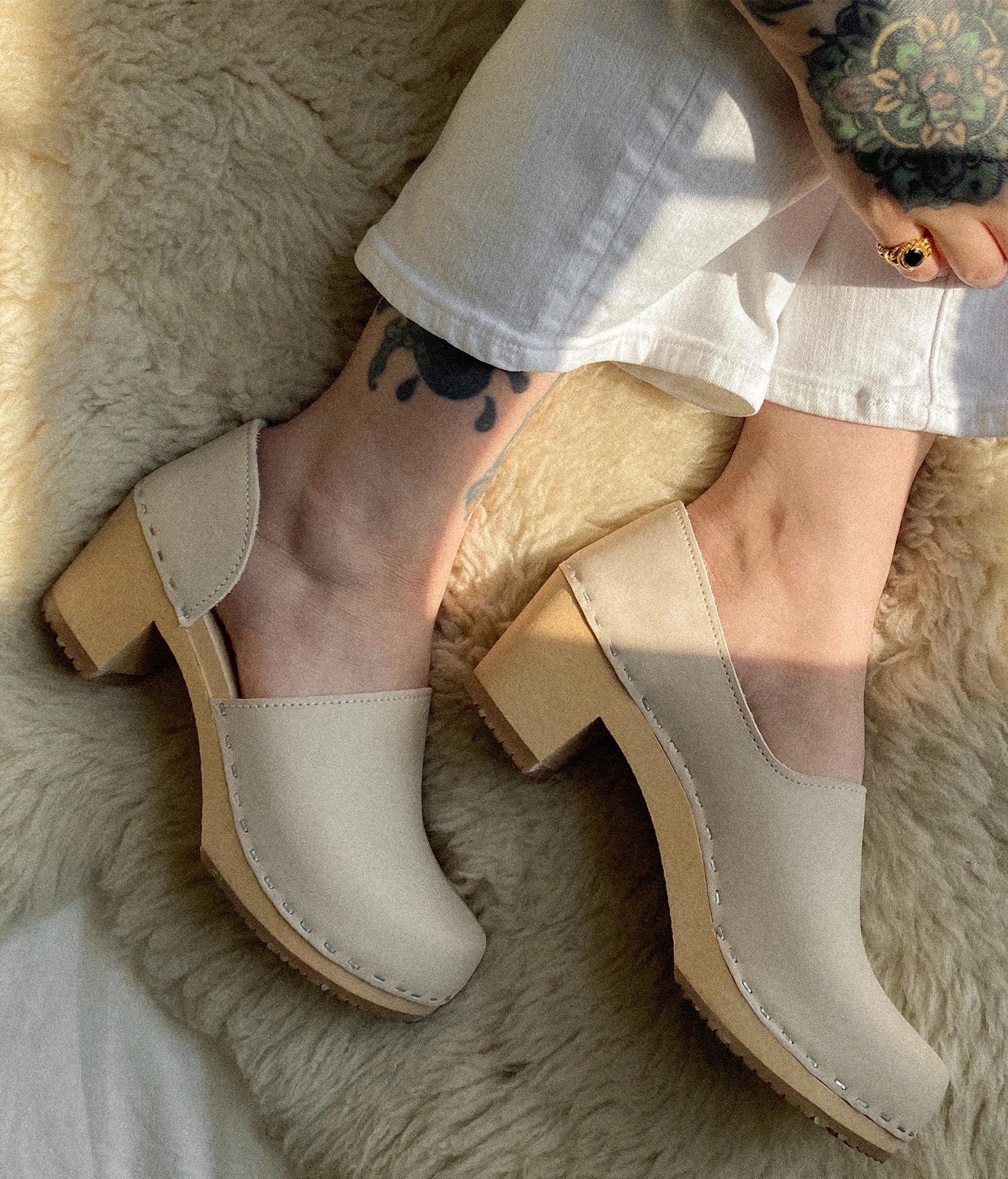 Beige clogs worn on a fluffy surface, high heeled closed-back clogs in sand white nubuck leather stapled on a light wooden base