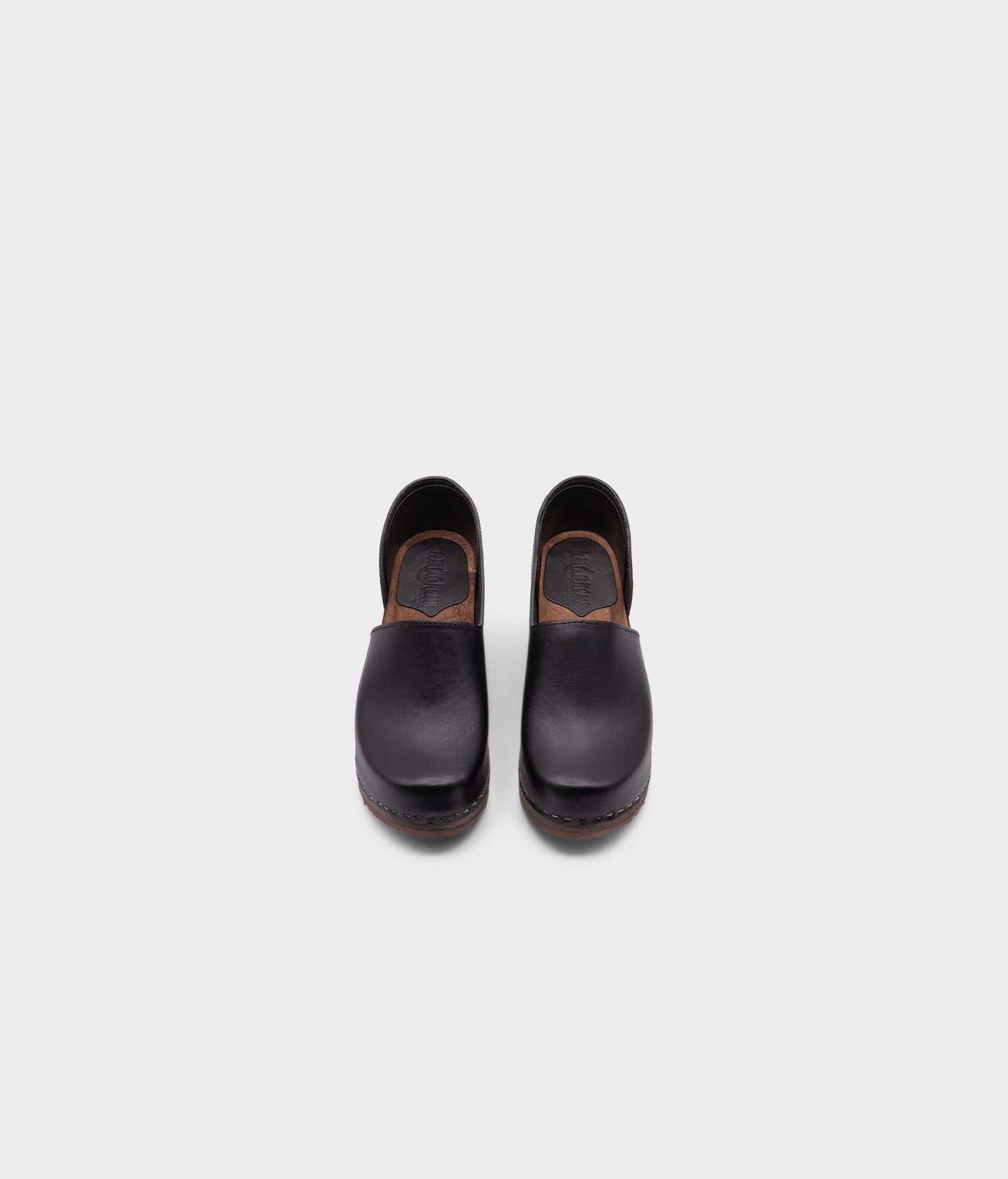 high heeled closed-back clogs in black vegetable tanned leather stapled on a dark wooden base