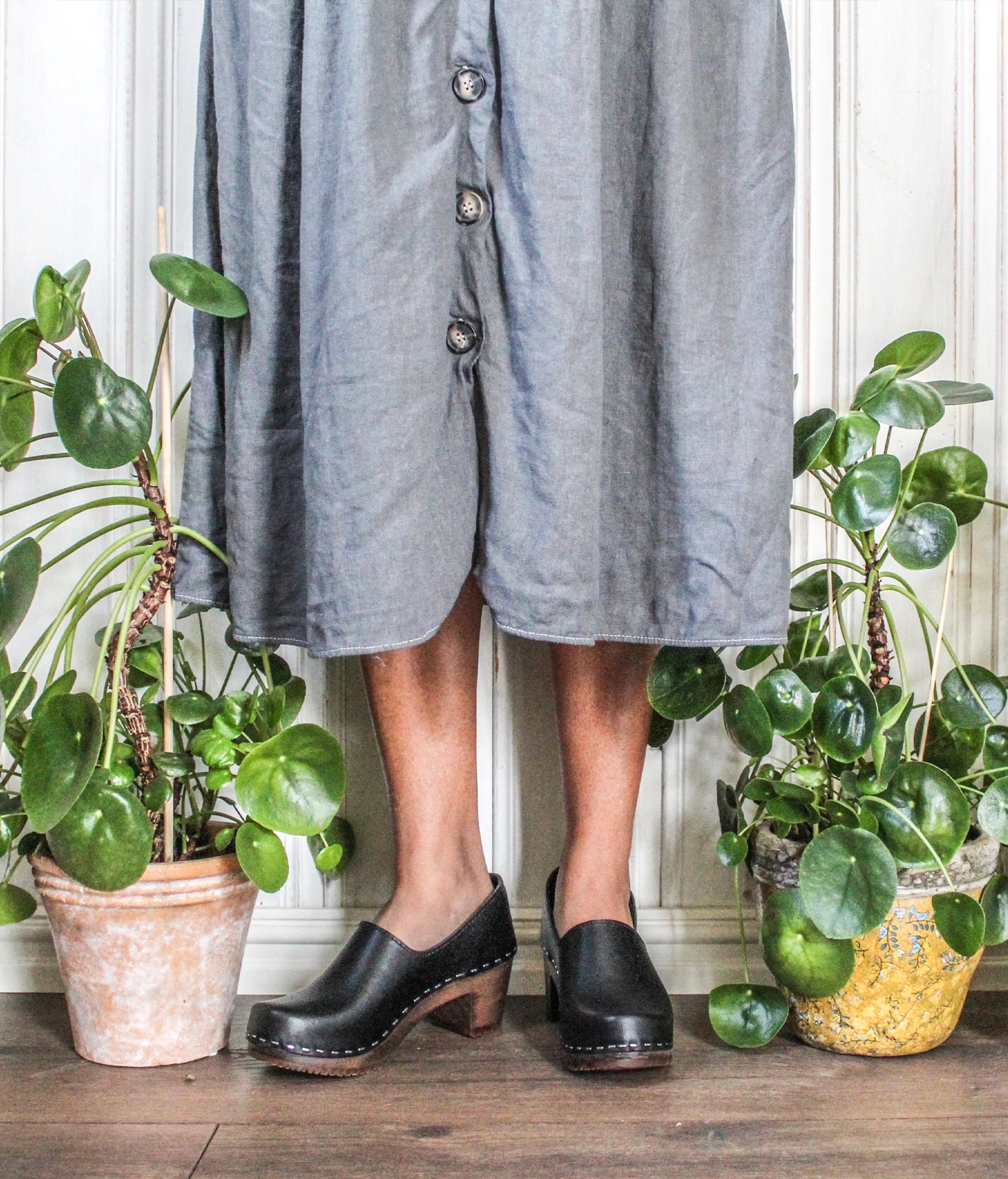 high heeled closed-back clogs in black vegetable tanned leather stapled on a dark wooden base